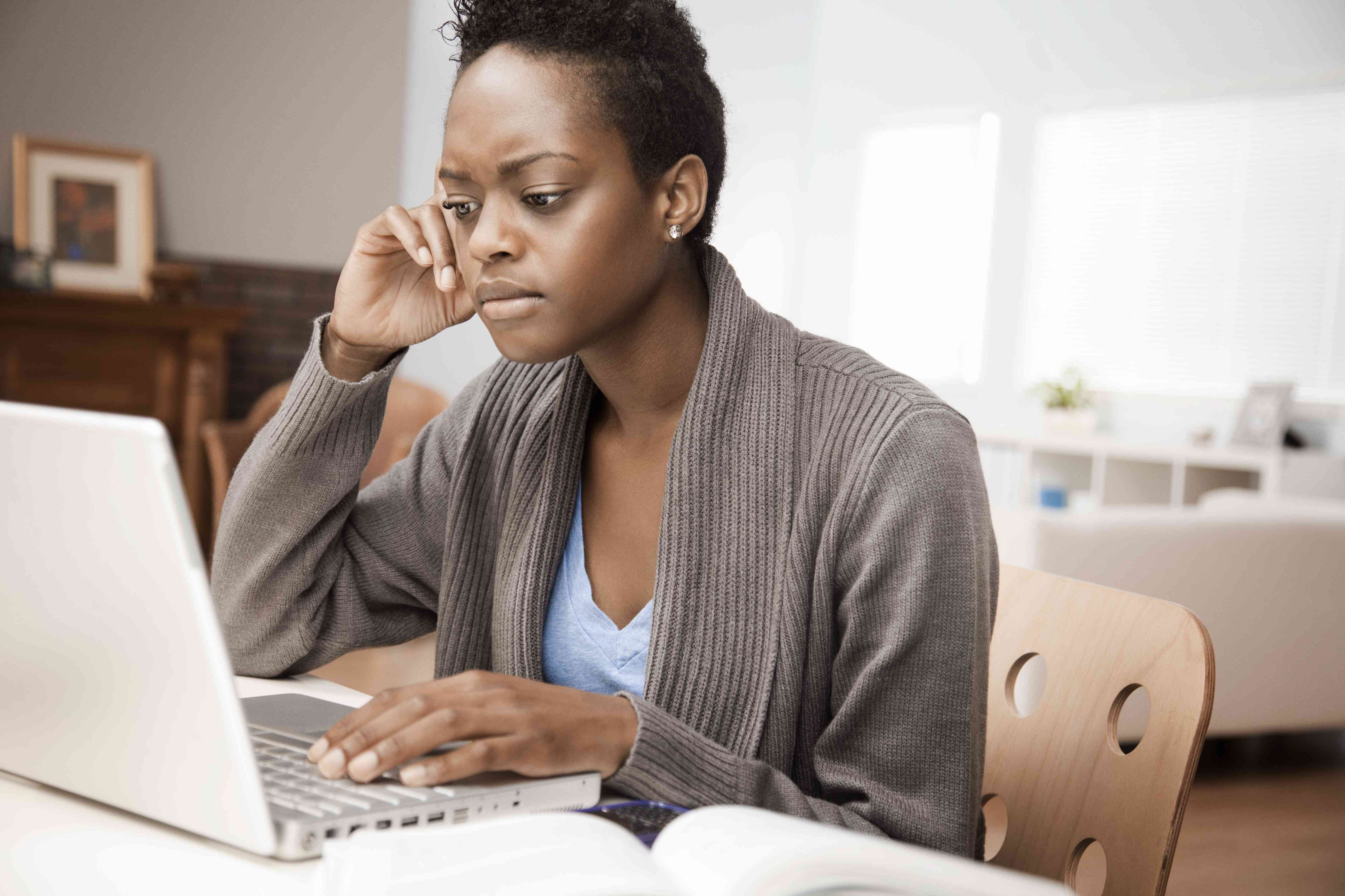 Young woman at her kitchen table intently studying her laptop