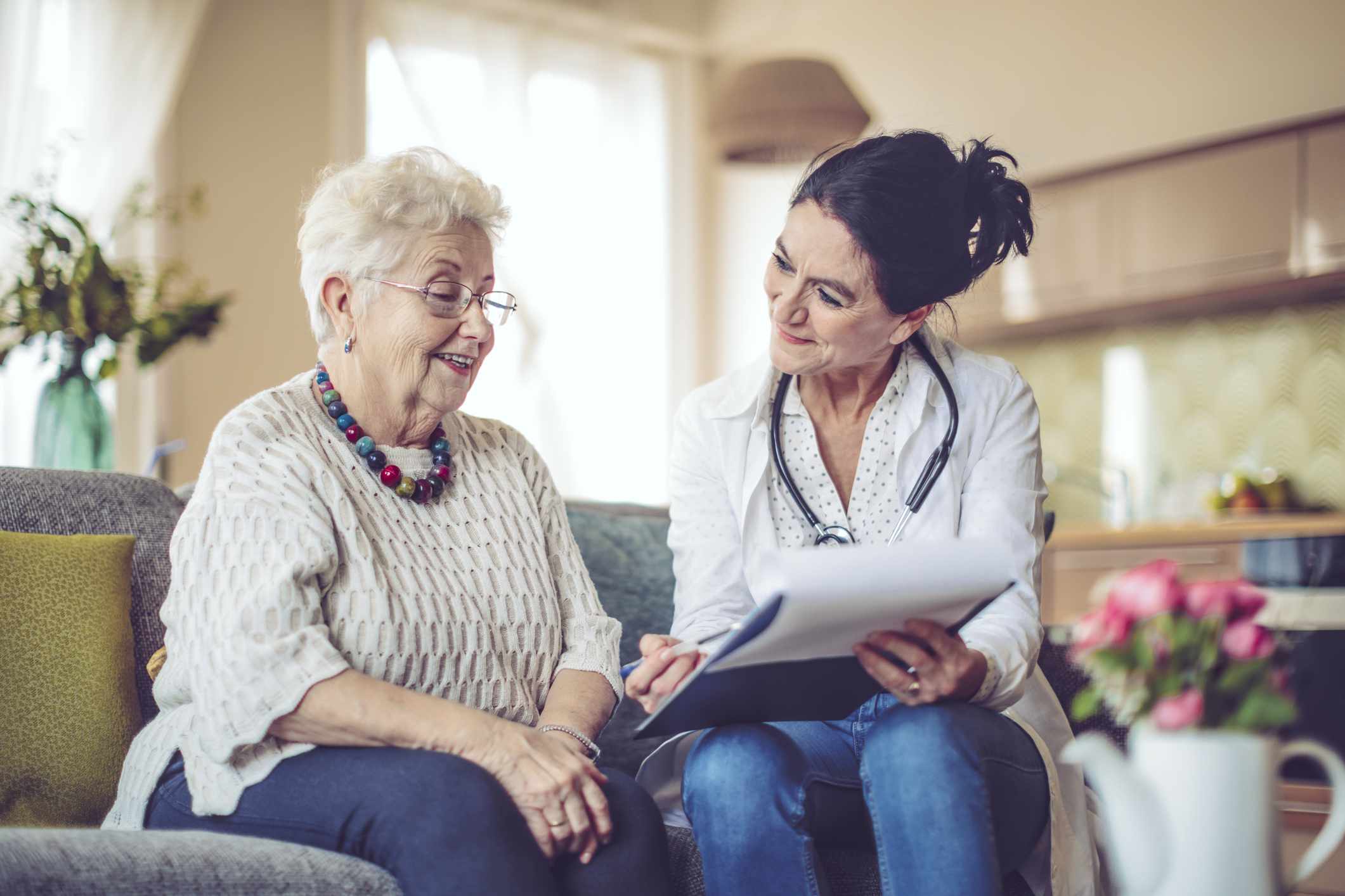 White-haired woman and nurse sit on a couch, going over paperwork