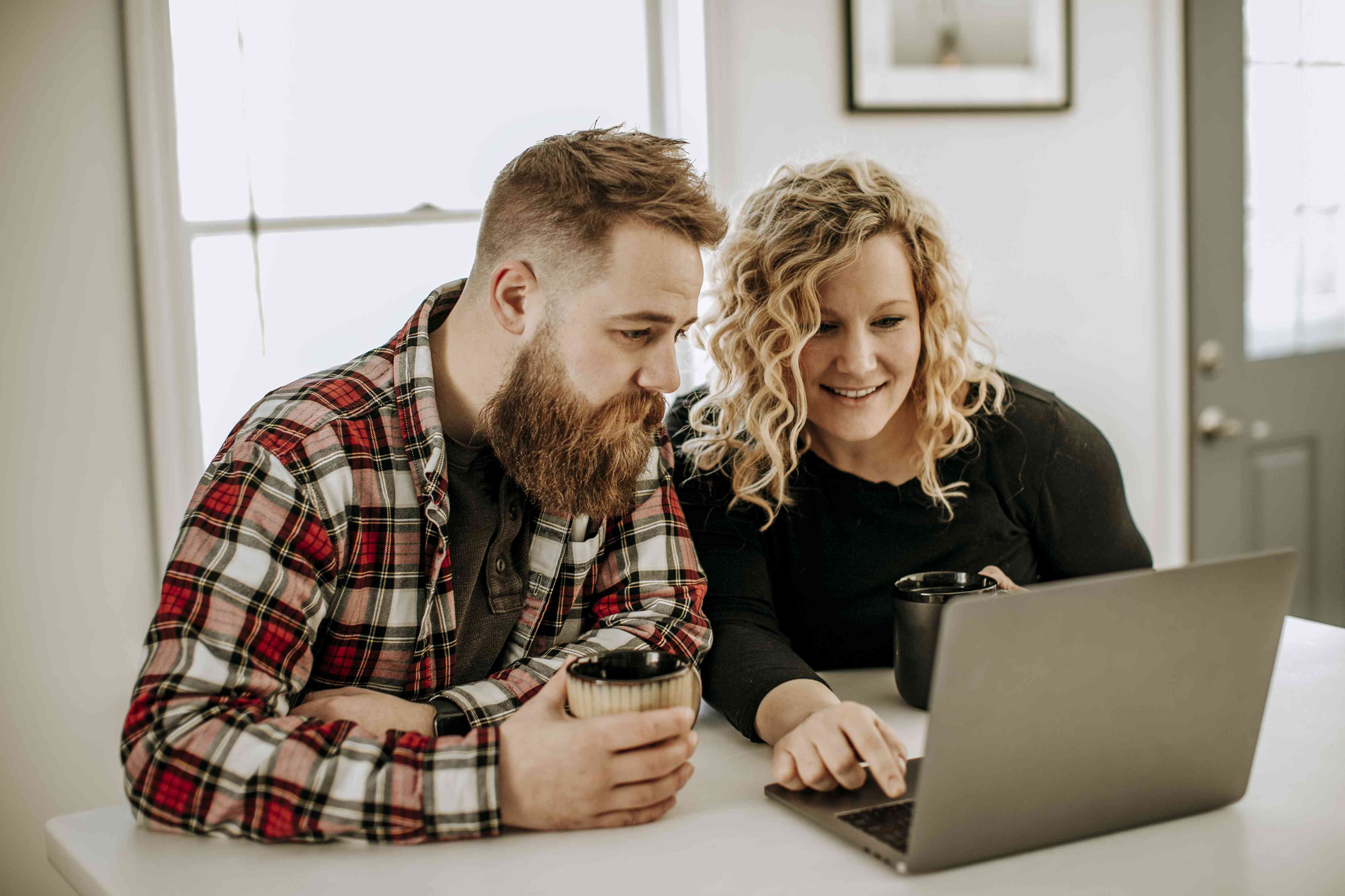 Young couople at kitchen table with coffee, looking happily together at their laptop