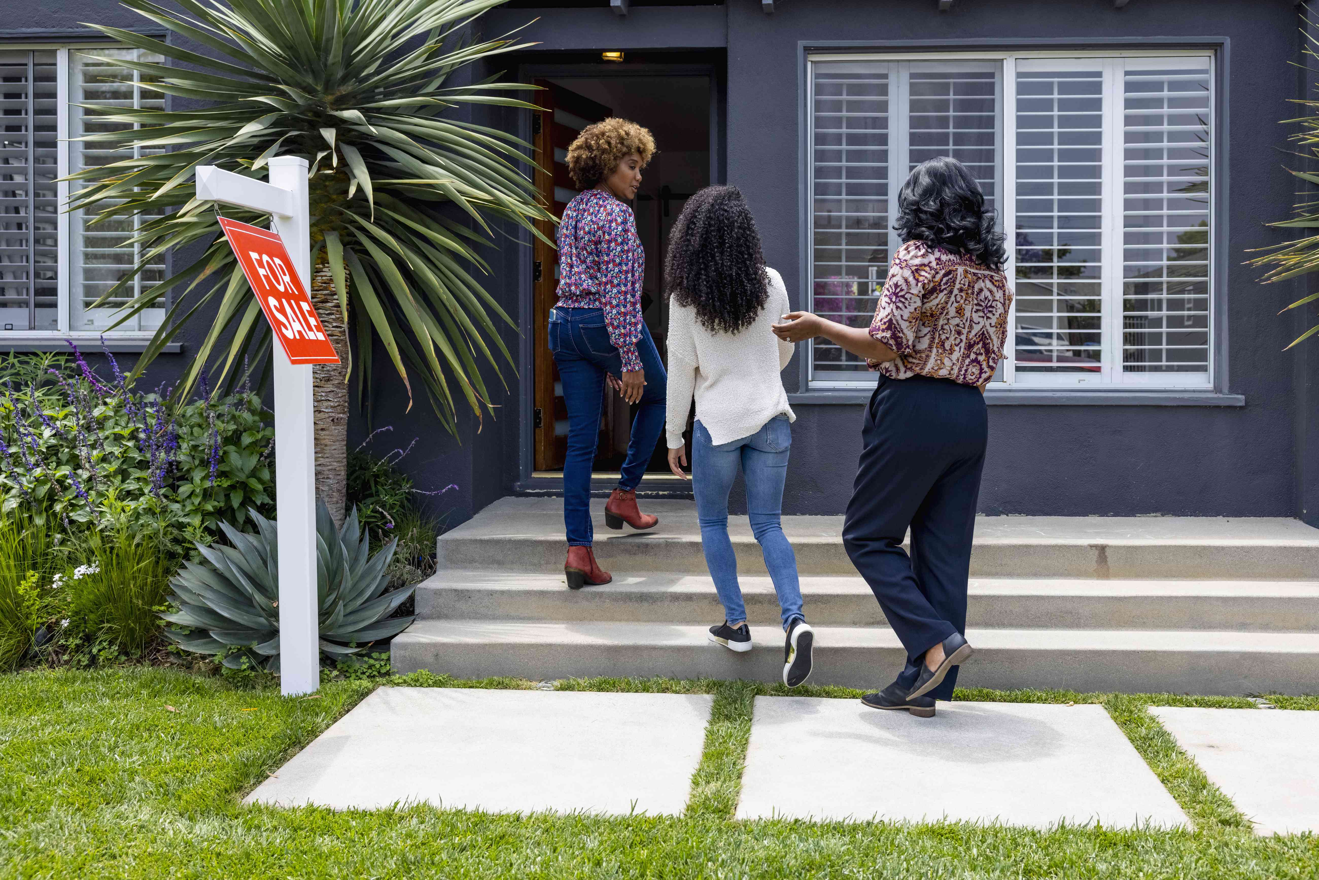 A realtor and two women walking up the steps to a house that is for sale