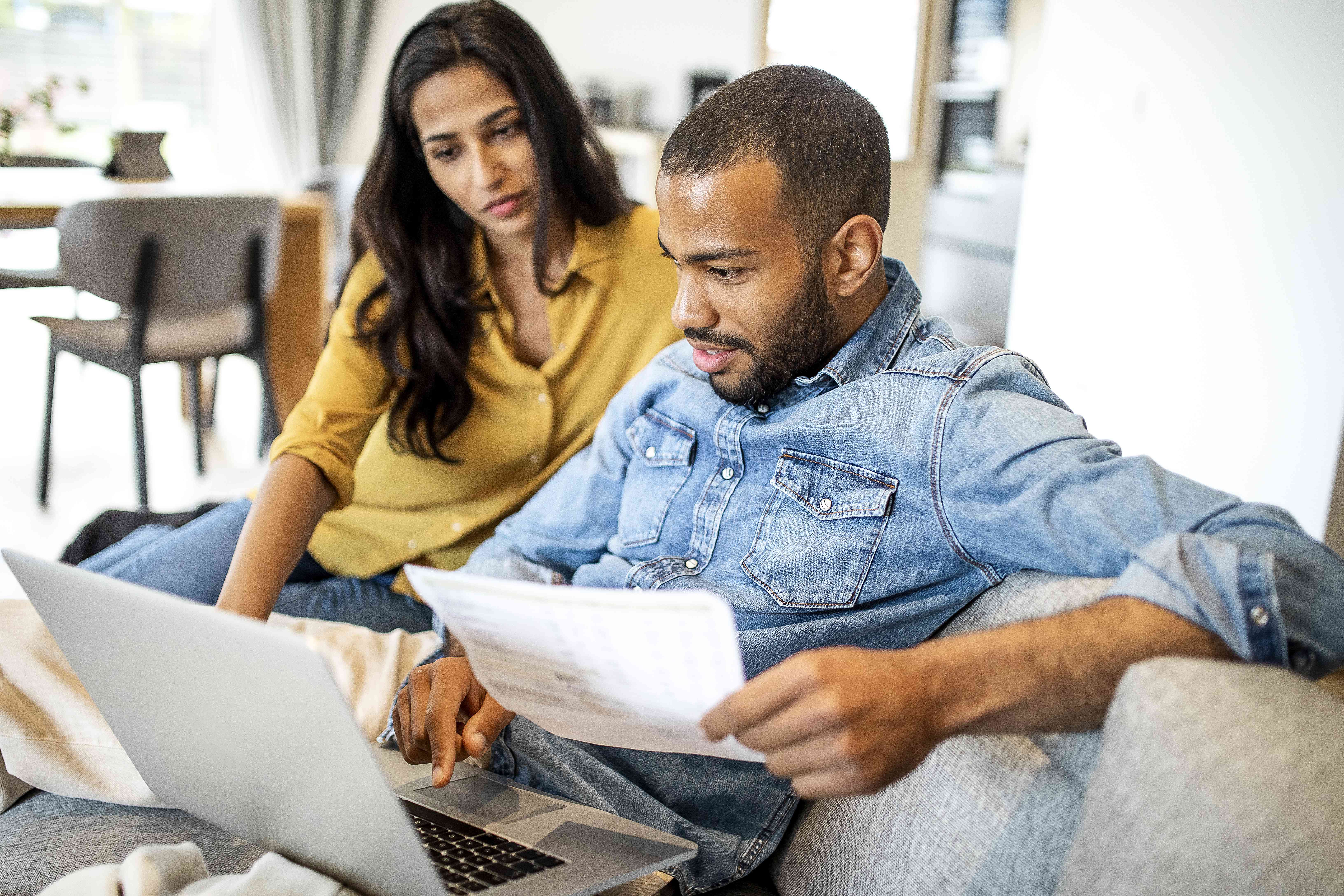 Young couple of color in their living room looking together at financial documents and a laptop