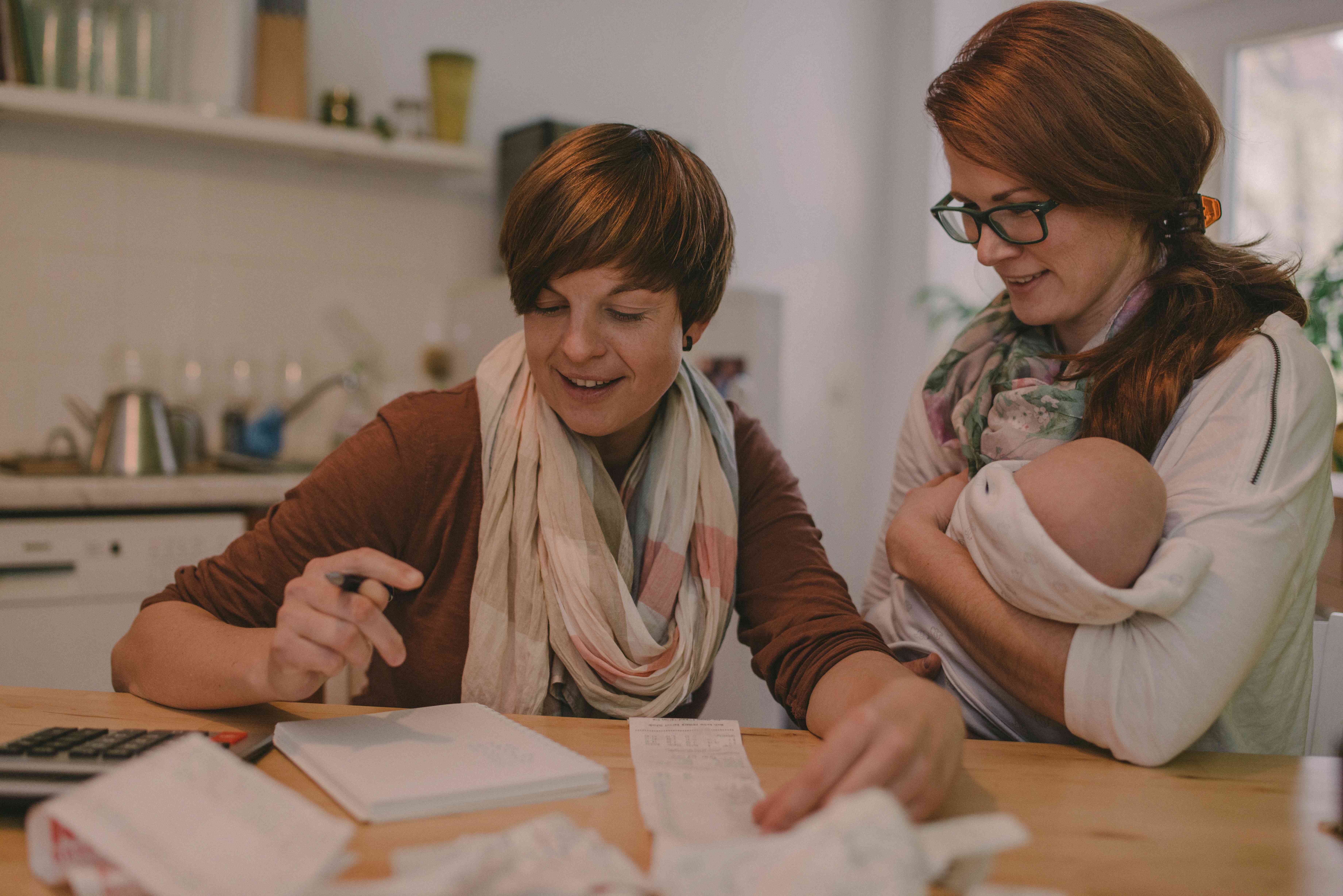 A couple does their household budget at home while one holds a newborn child.