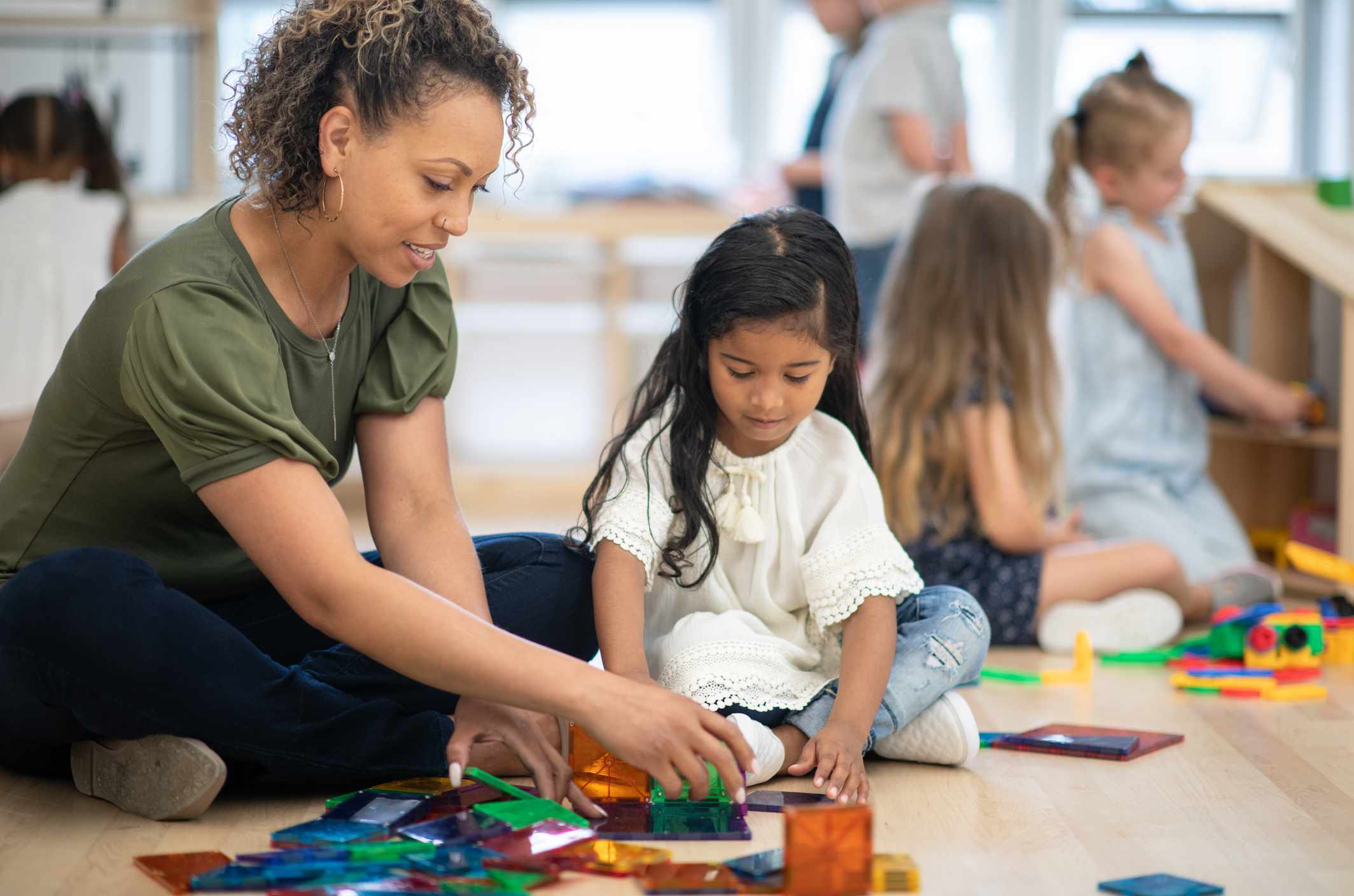 A child care center with an adult and kids seated on the floor and involved in projects.