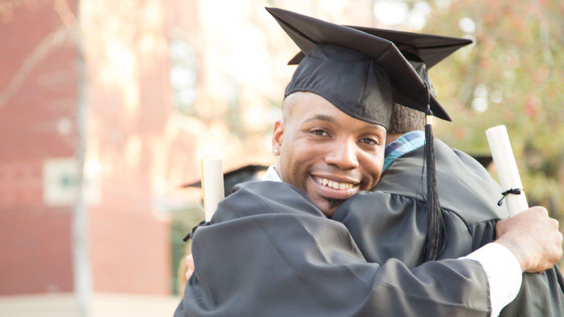 Black college graduate, with diploma, hugging friend