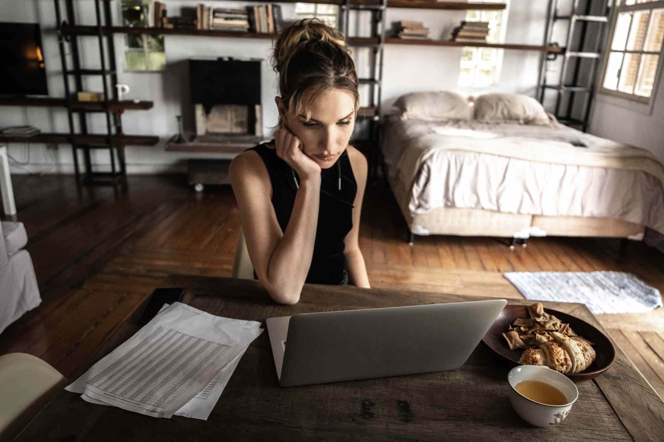 Woman working on laptop at home studio with pastries and coffee