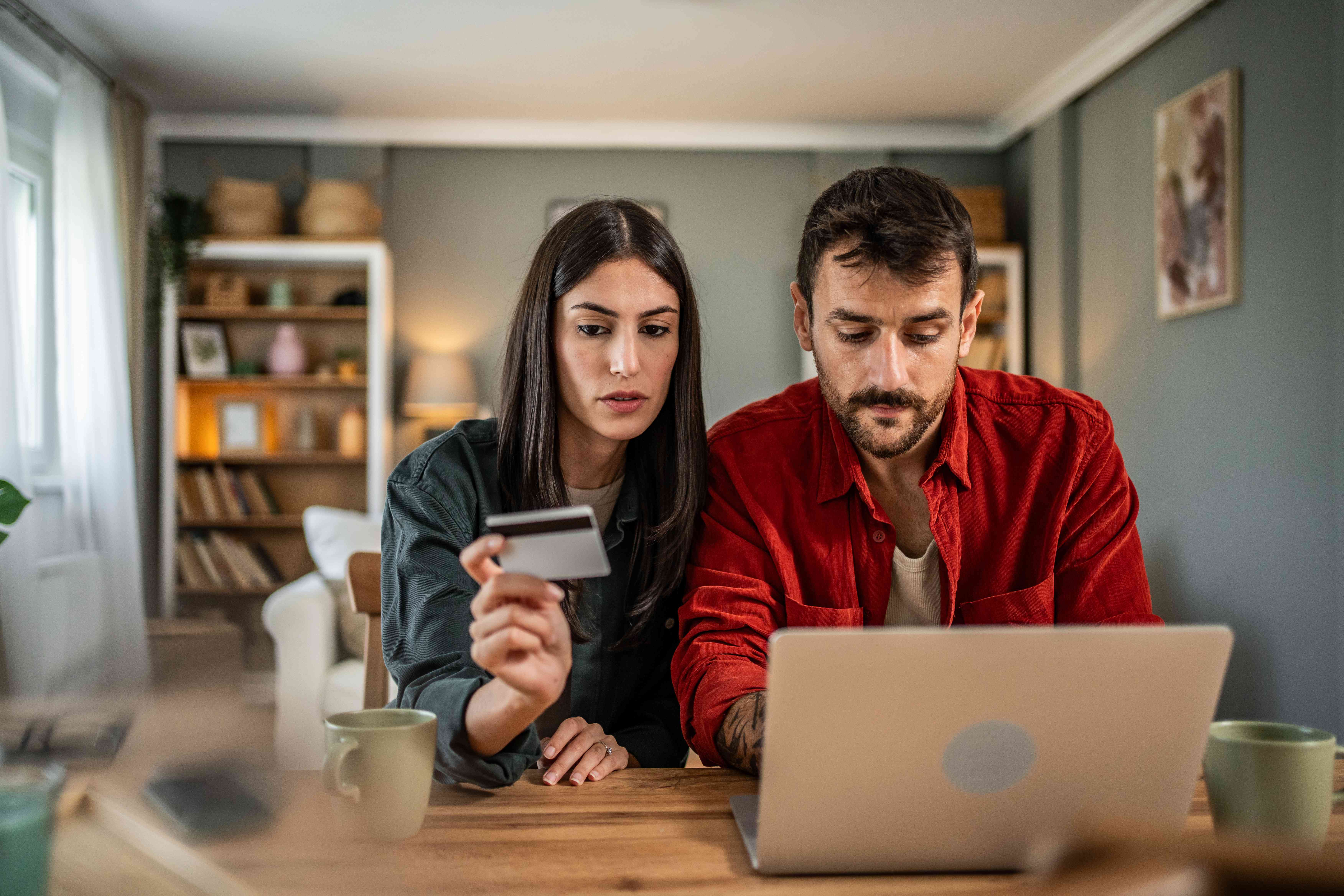 A man and a woman sit at a table with a laptop and look at a credit card