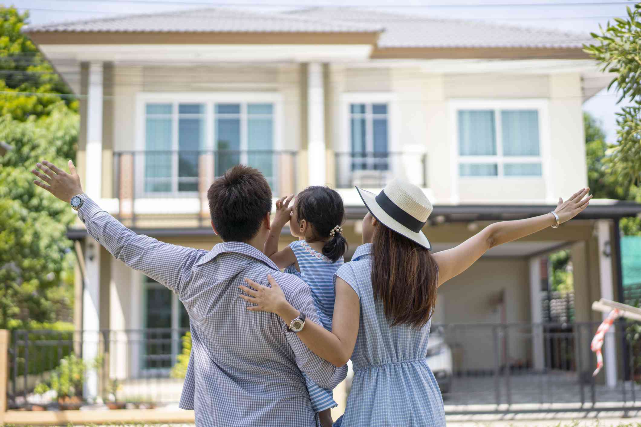 Young parents holding a young child with their arms opened towards a house