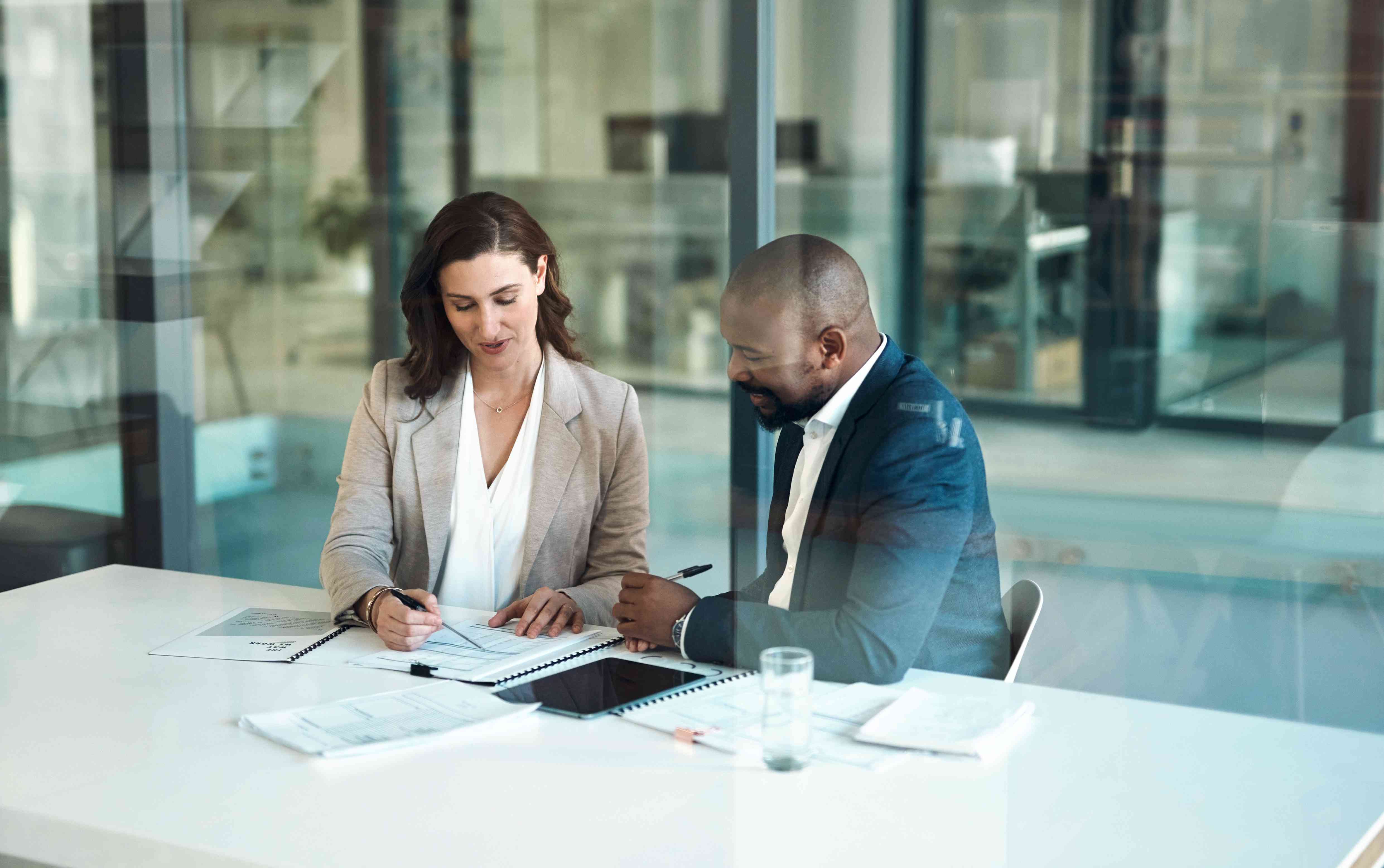 Two people sit at an office table reviewing financial documents.