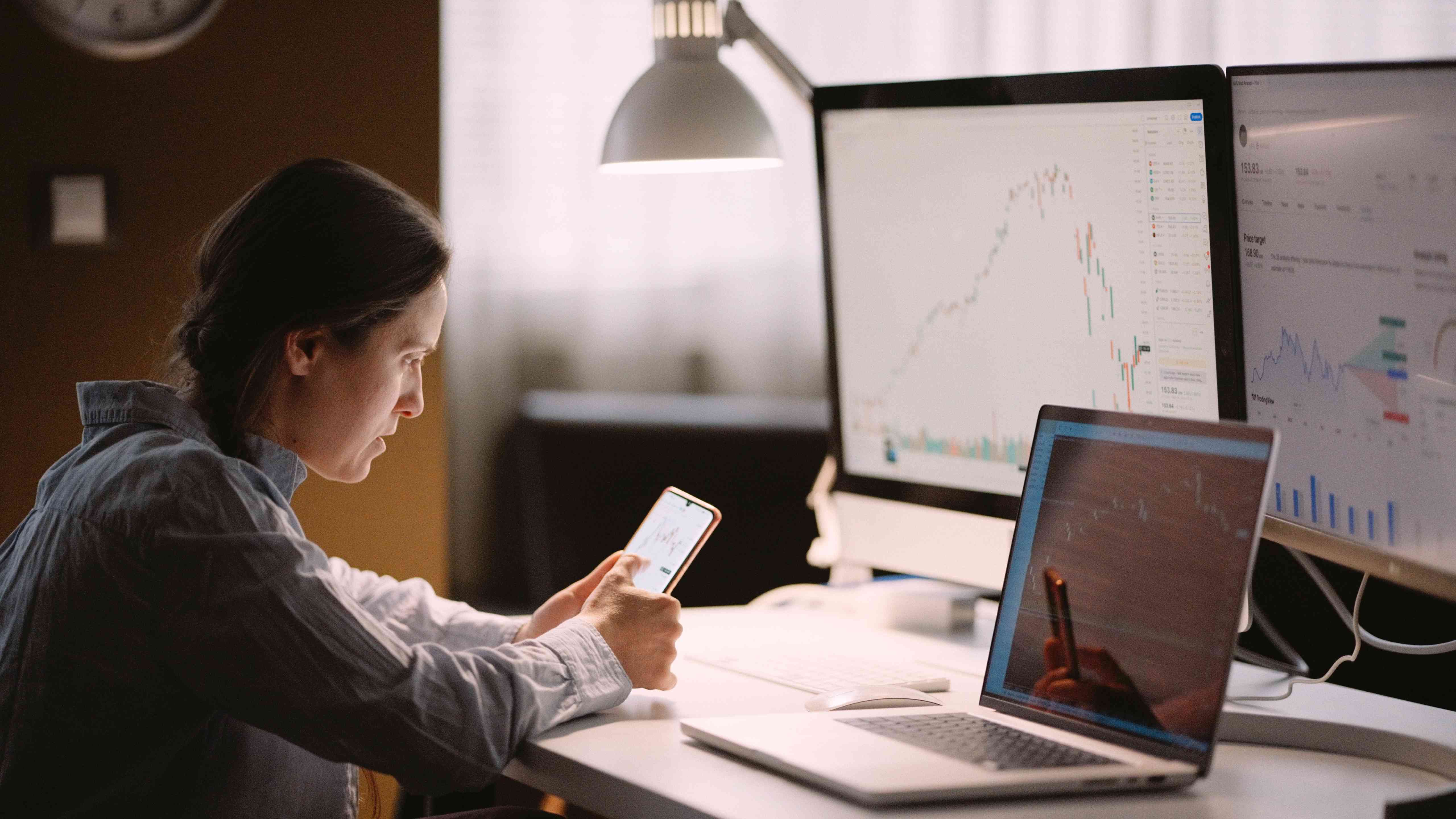 Woman studying stock markets on TradingView app, checking on trading positions and stock markets in the evening at home.