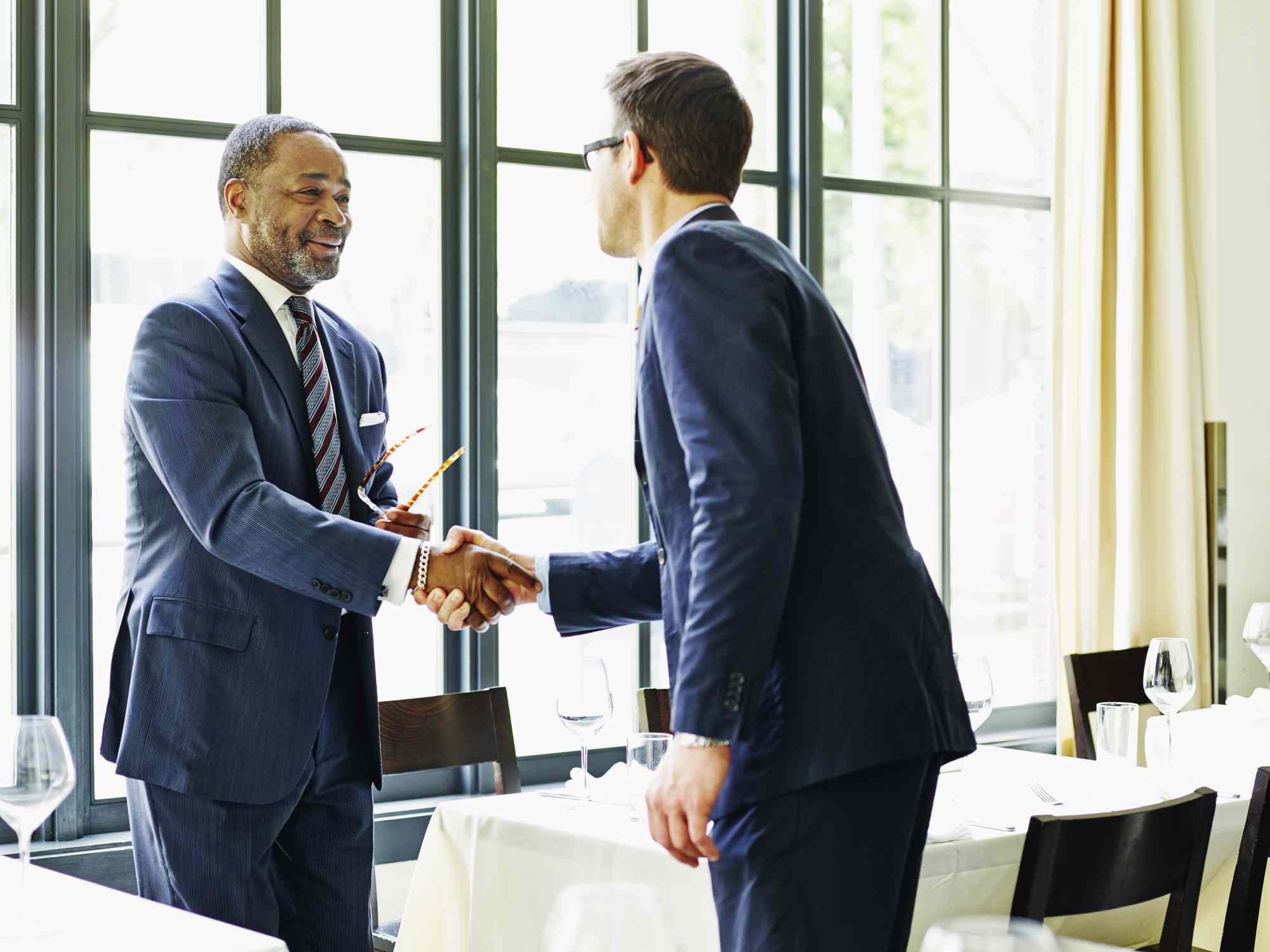 Two people in suits shaking hands in a restaurant