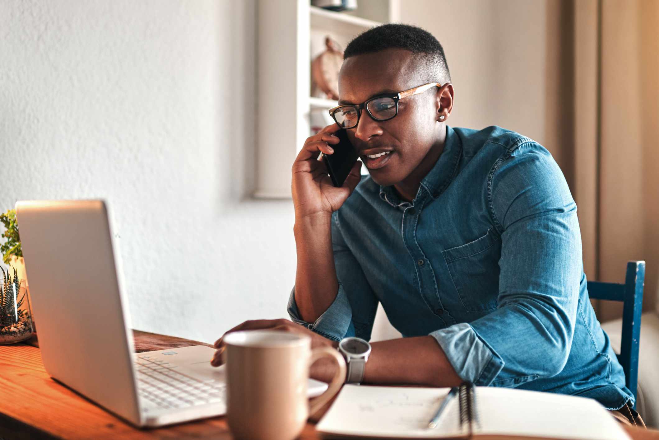 person in blue jean shirt on computer at wooden table