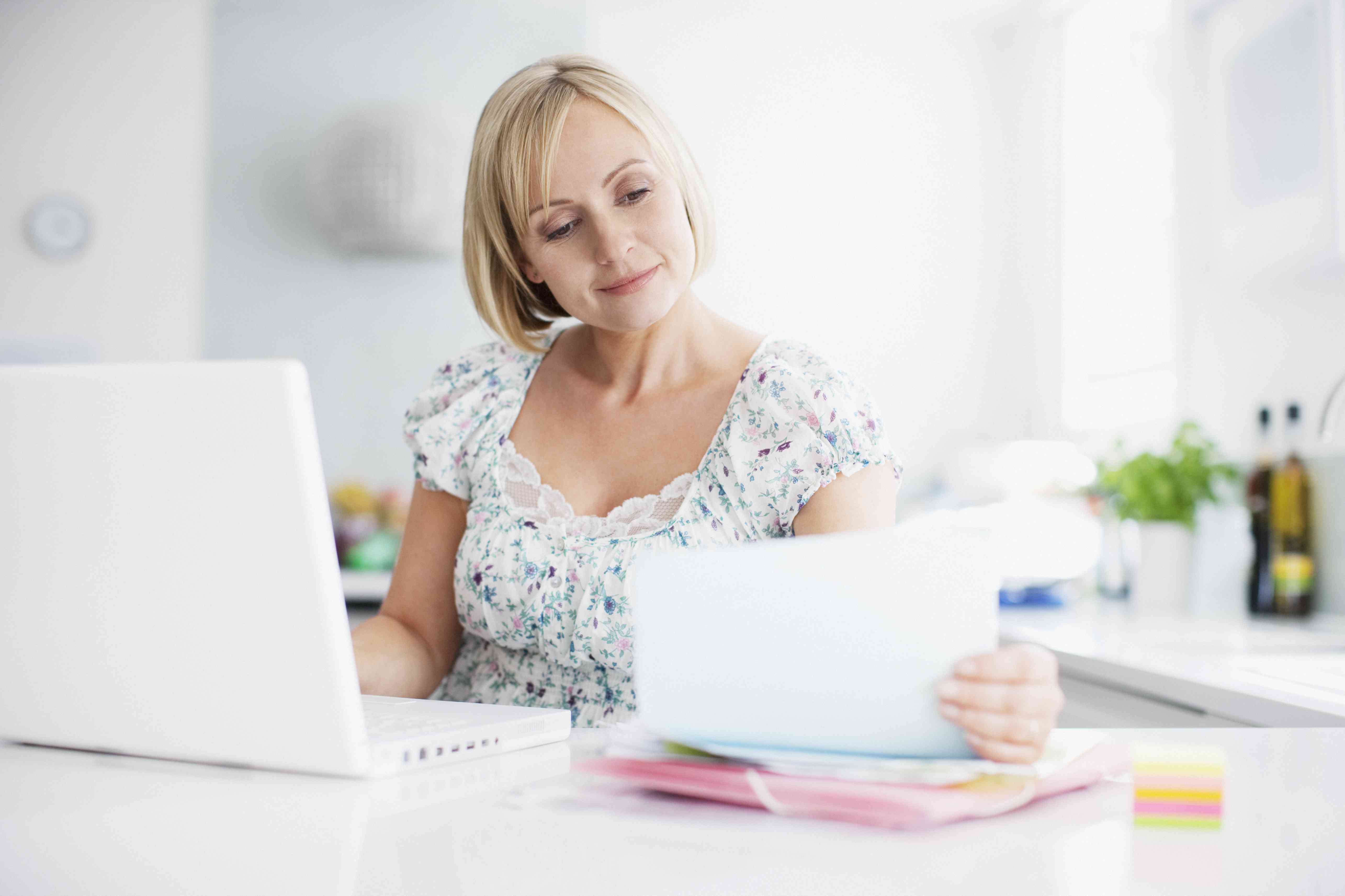 Woman looking at papers while on laptop