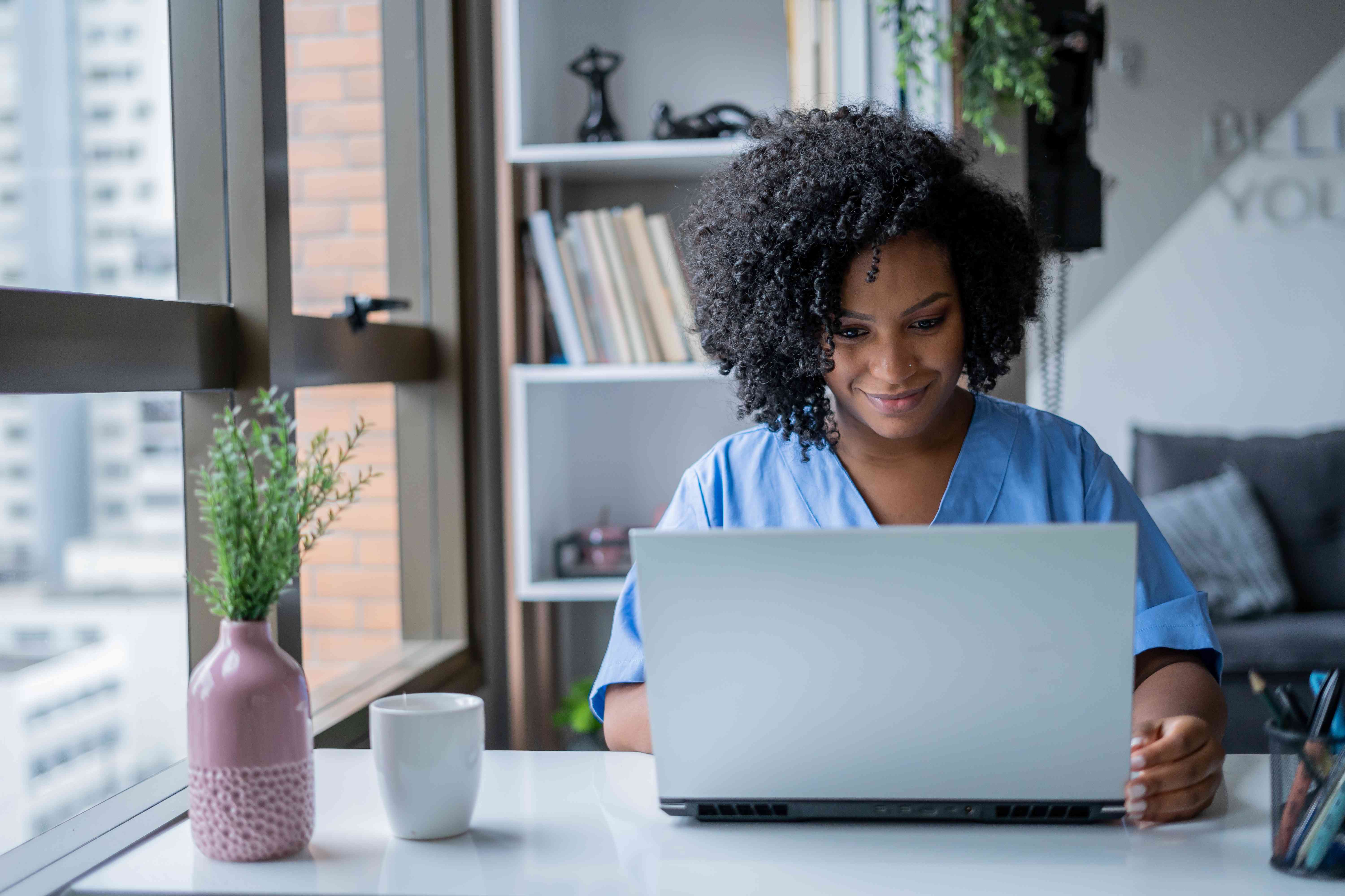 Young woman at home in her living room, looking at her laptop with a smile