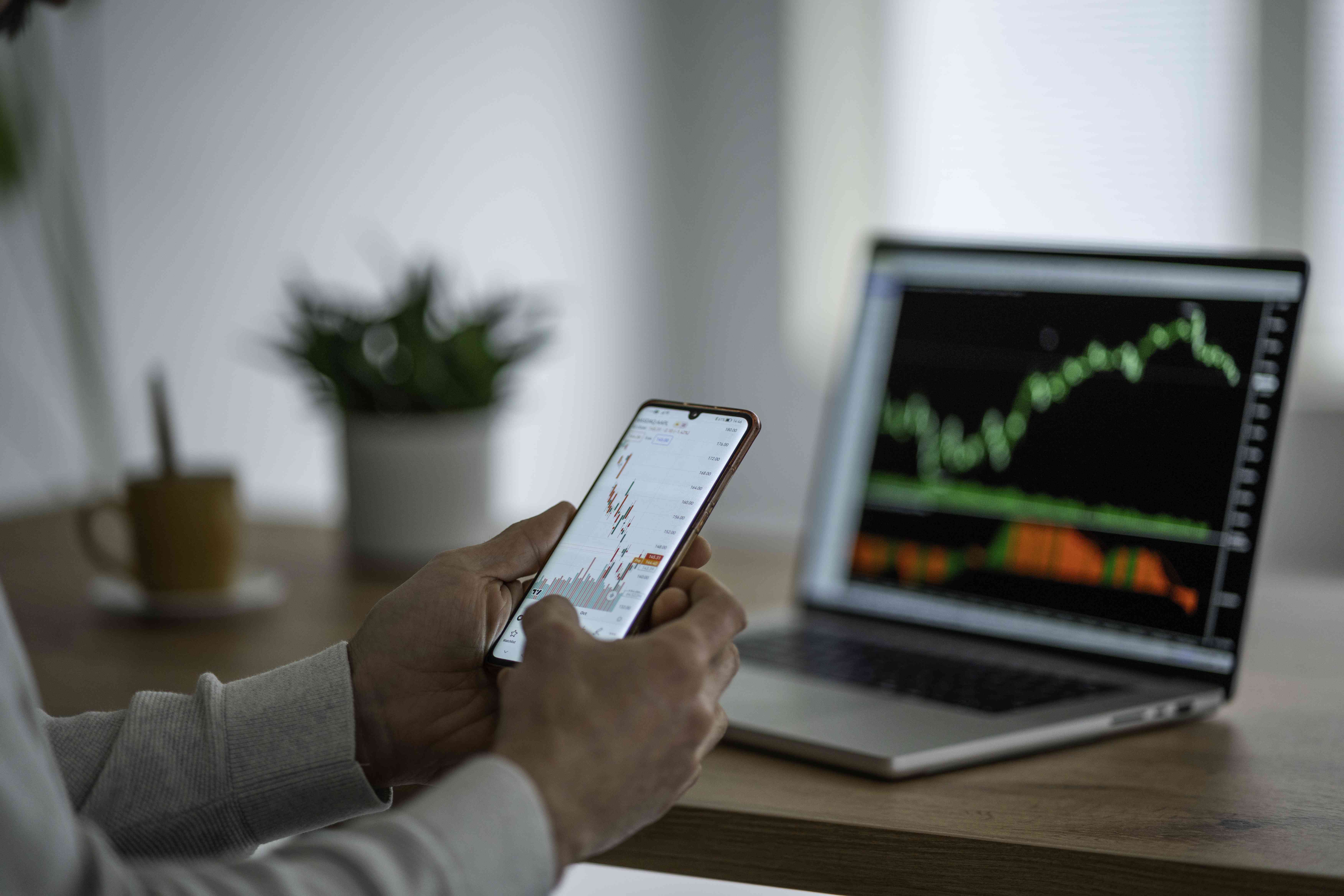 A person sitting at a desk and using a smart phone to trade stocks