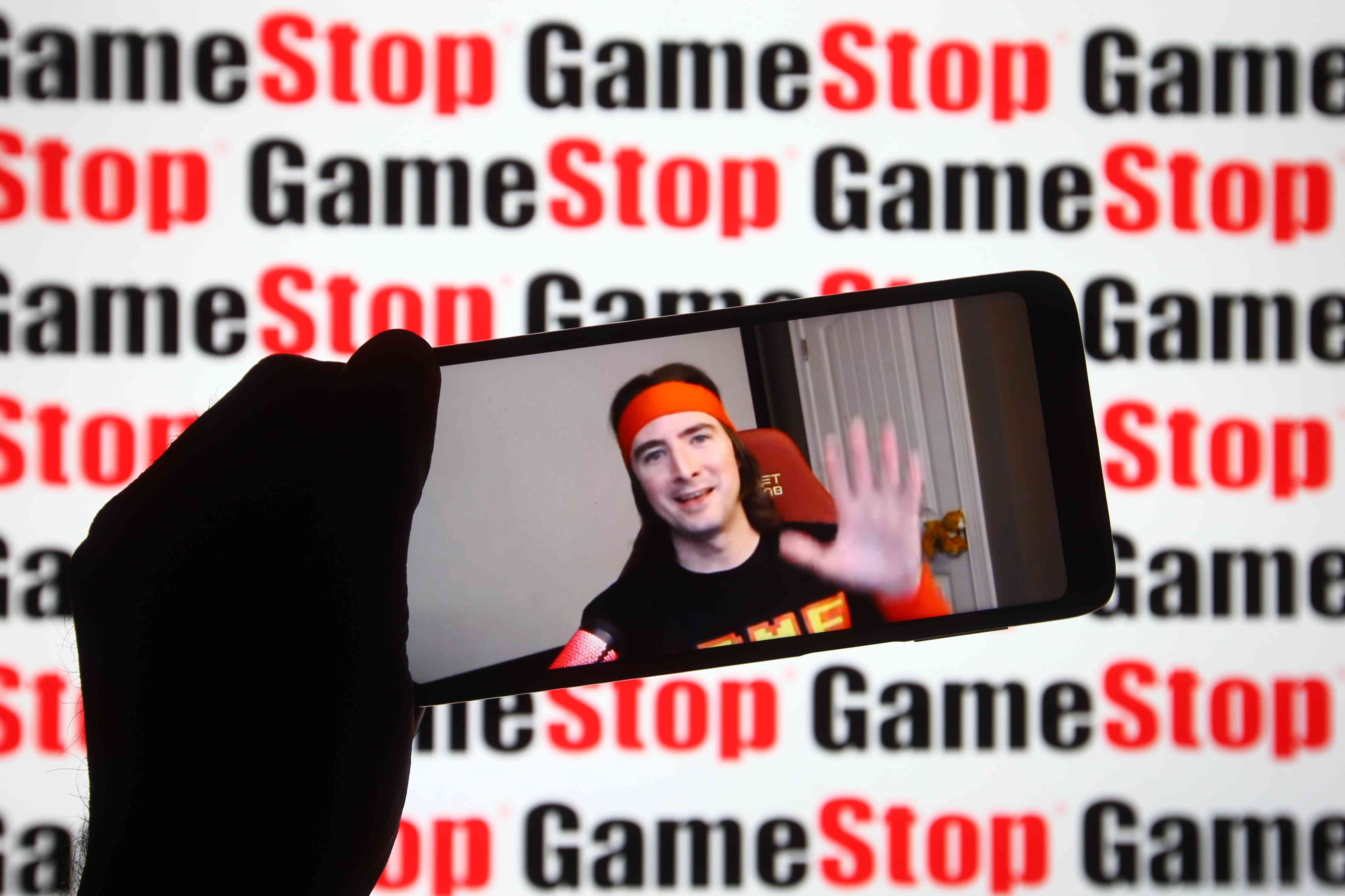 Keith Gill, known on Reddit under the pseudonym Roaring Kitty, is seen on a fragment of a YouTube video displayed on a smartphone screen in front of the GameStop logo