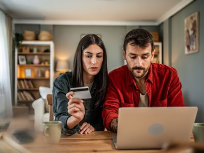 A man and a woman sit at a table with a laptop and look at a credit card