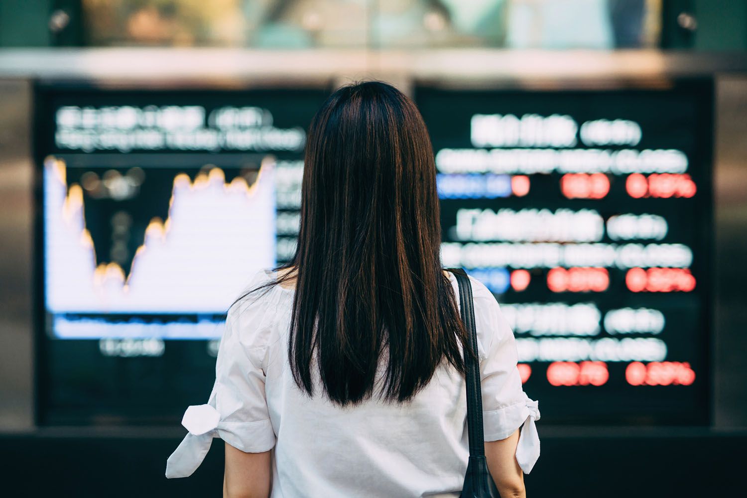 Rear view of businesswoman looking at stock exchange market display screen board in downtown financial district