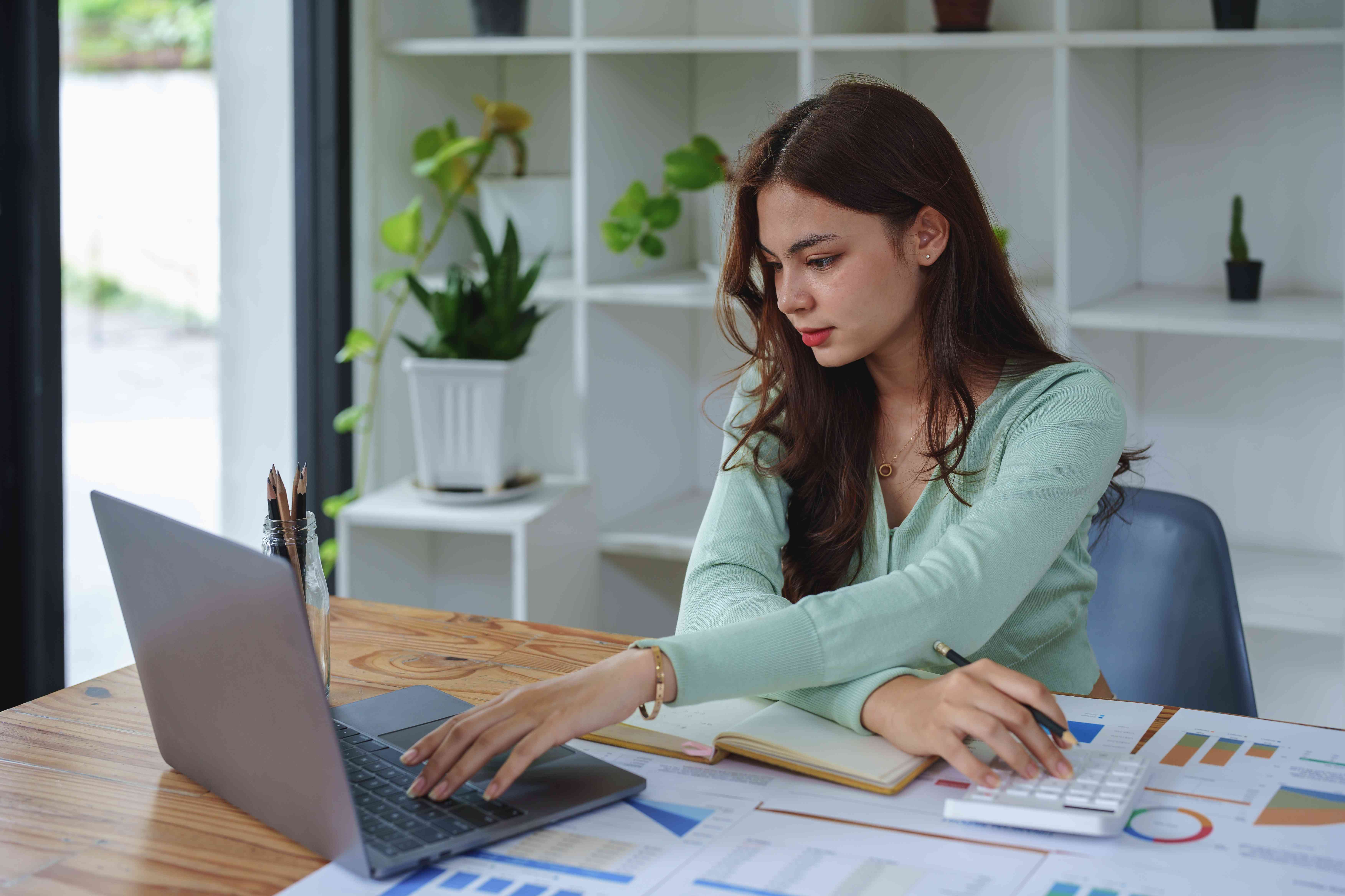 Young female entrepreneurs using laptop and calculator at her desk