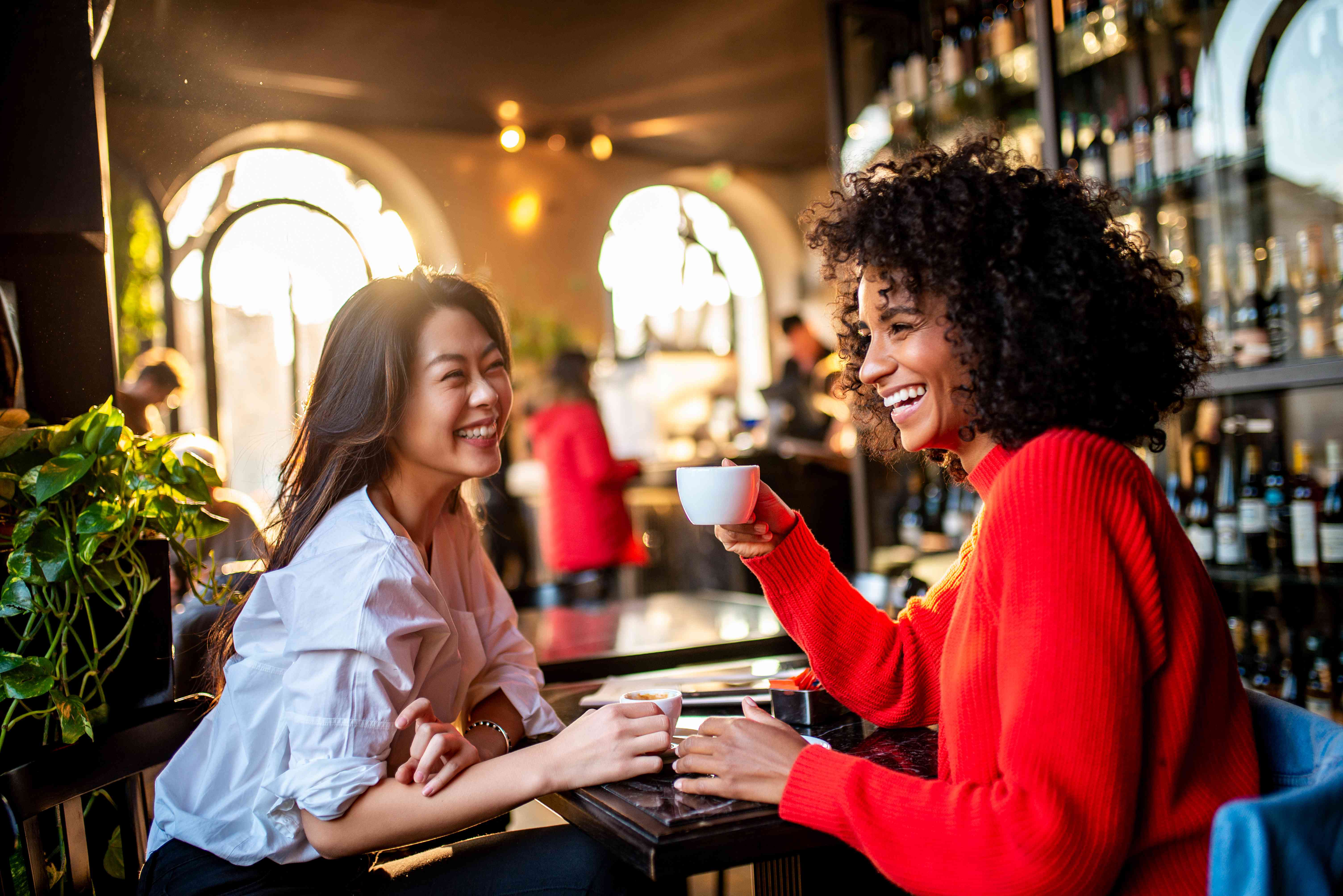 Two women sit at a cafe in Europe sipping coffee