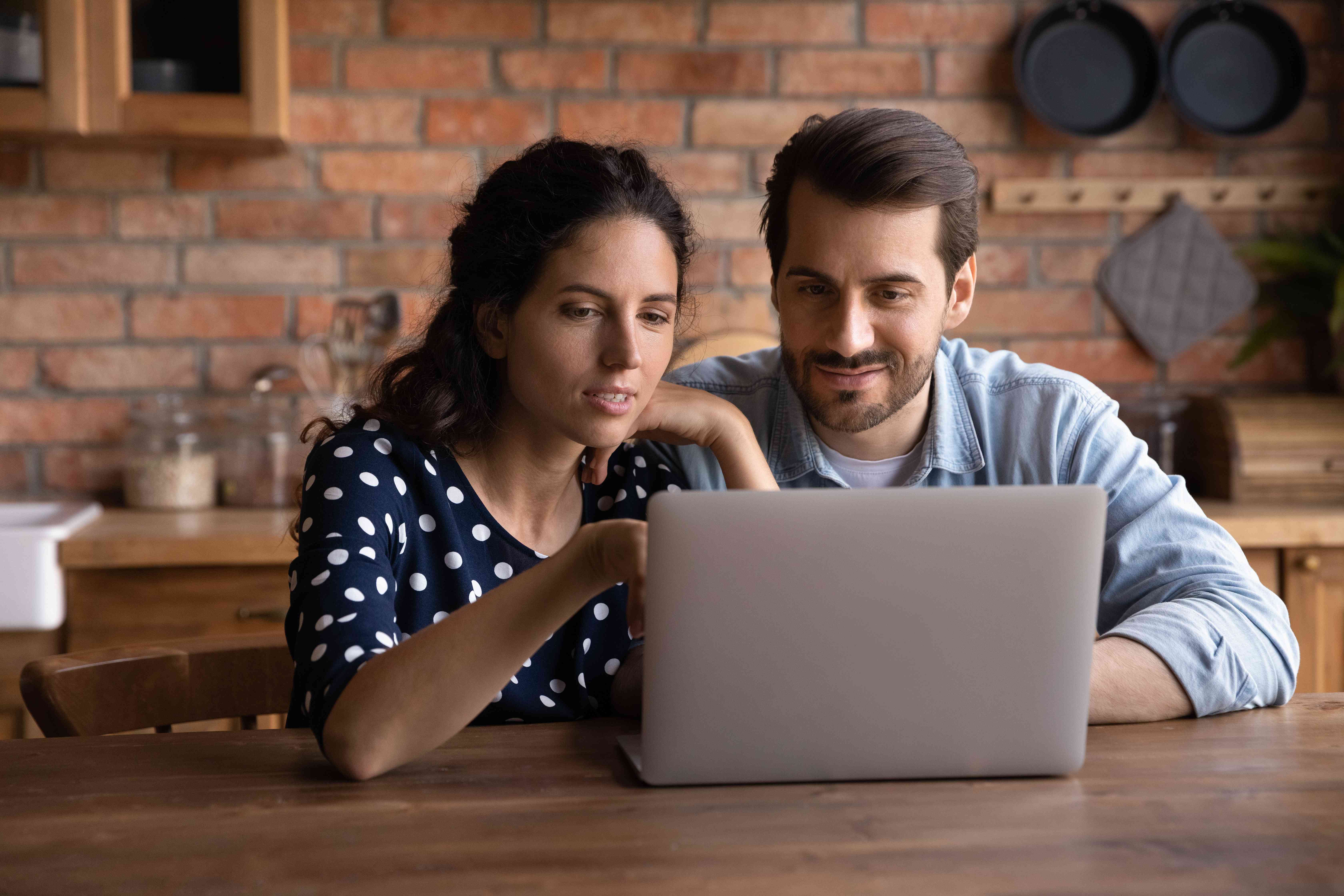 Millennial couple sitting in kitchen and looking together at their laptop