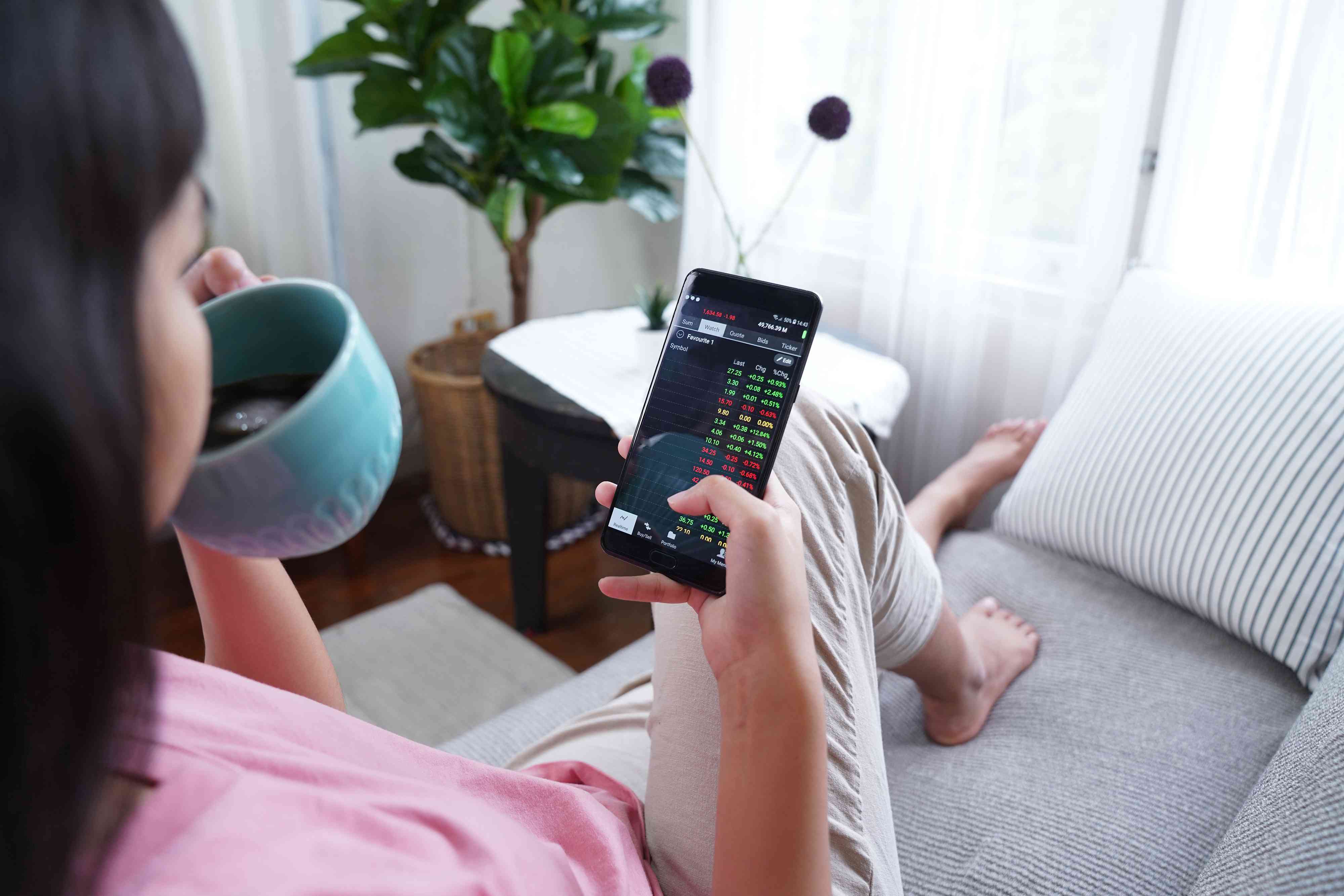 Woman checking stocks trading data via trading application on mobile phone