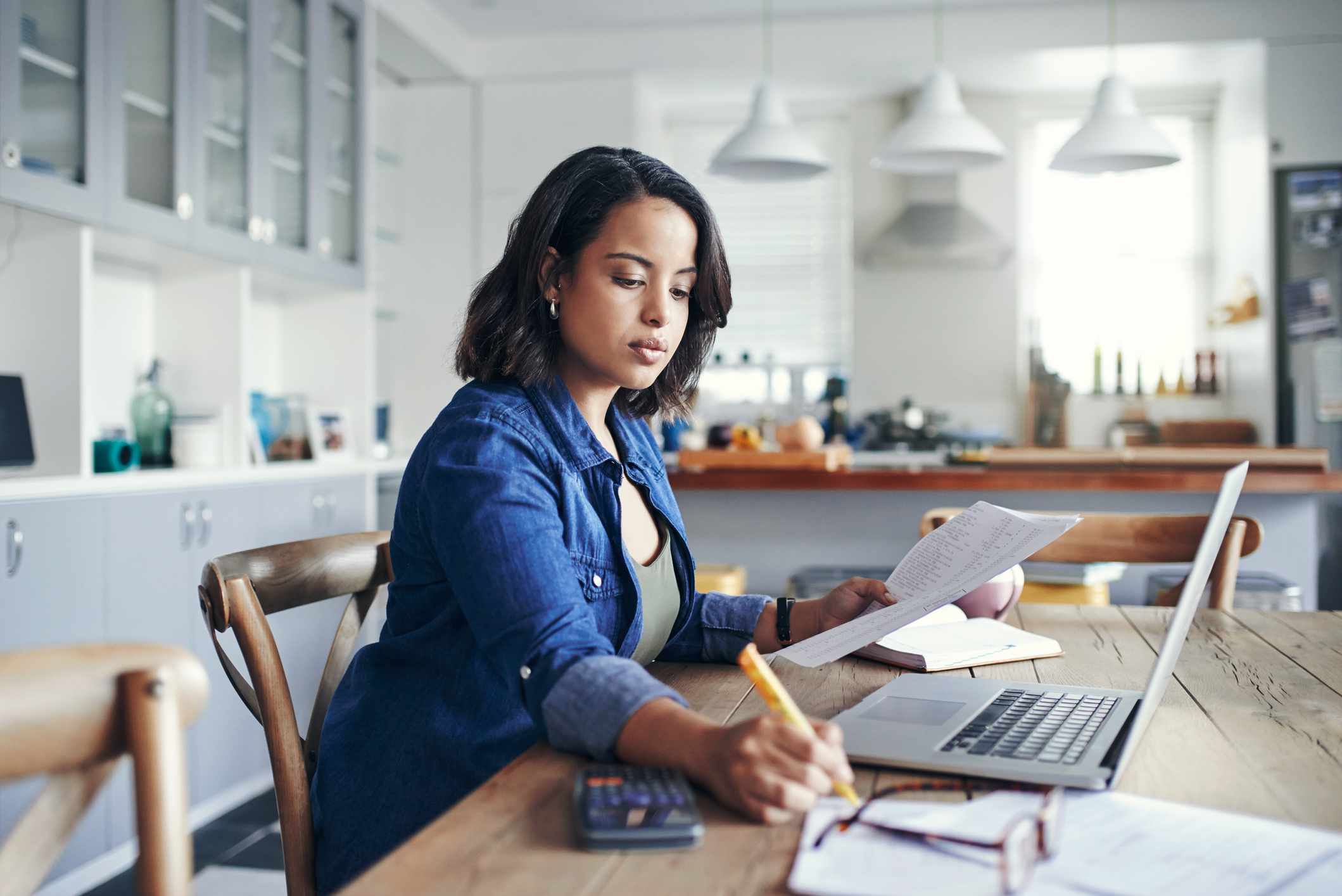 A young woman sitting at her kitchen table with a laptop and papers