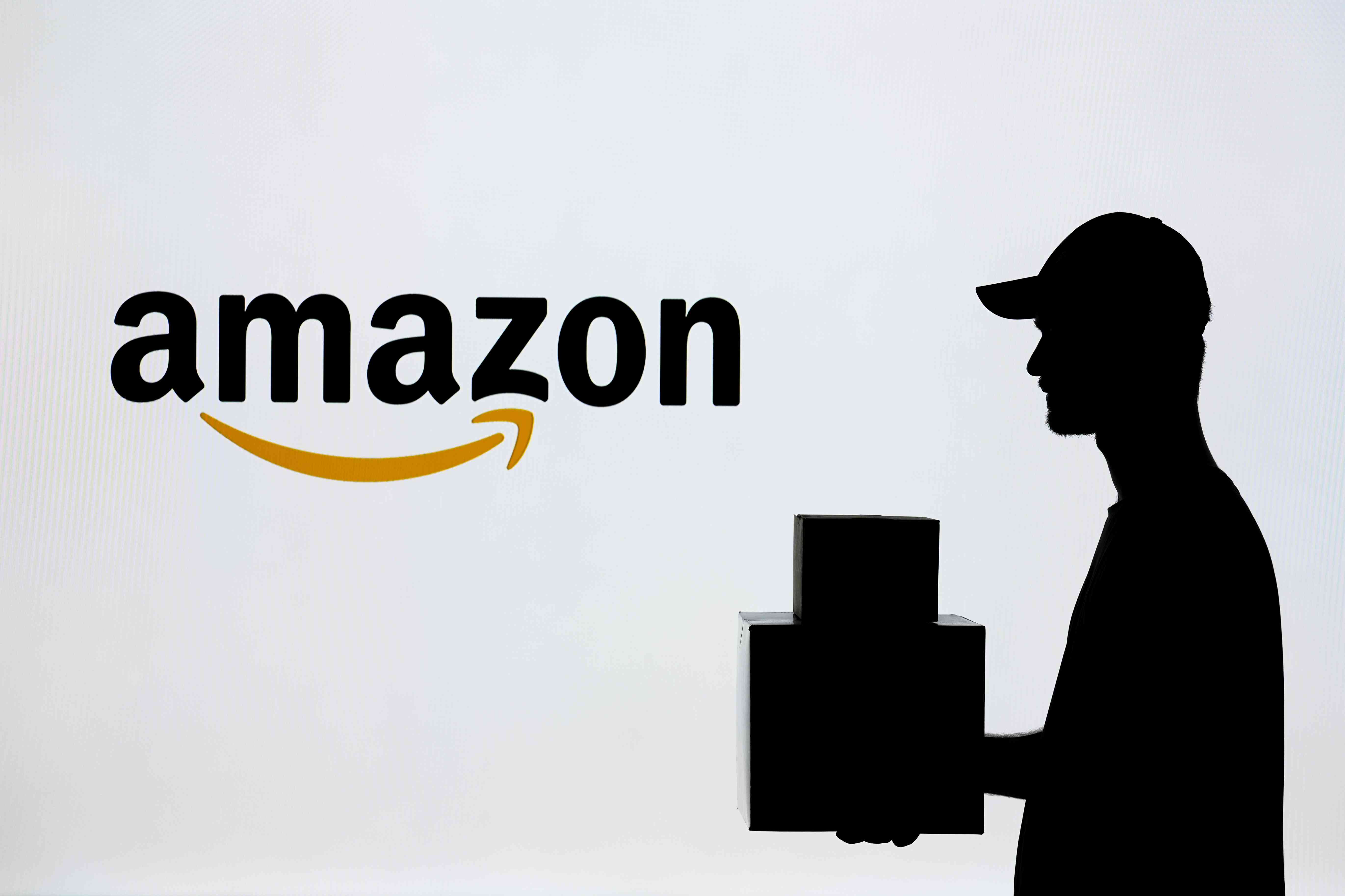 In this photo illustration a man carrying a package in front of the Amazon logo in Ankara, Turkiye on July 4, 2024