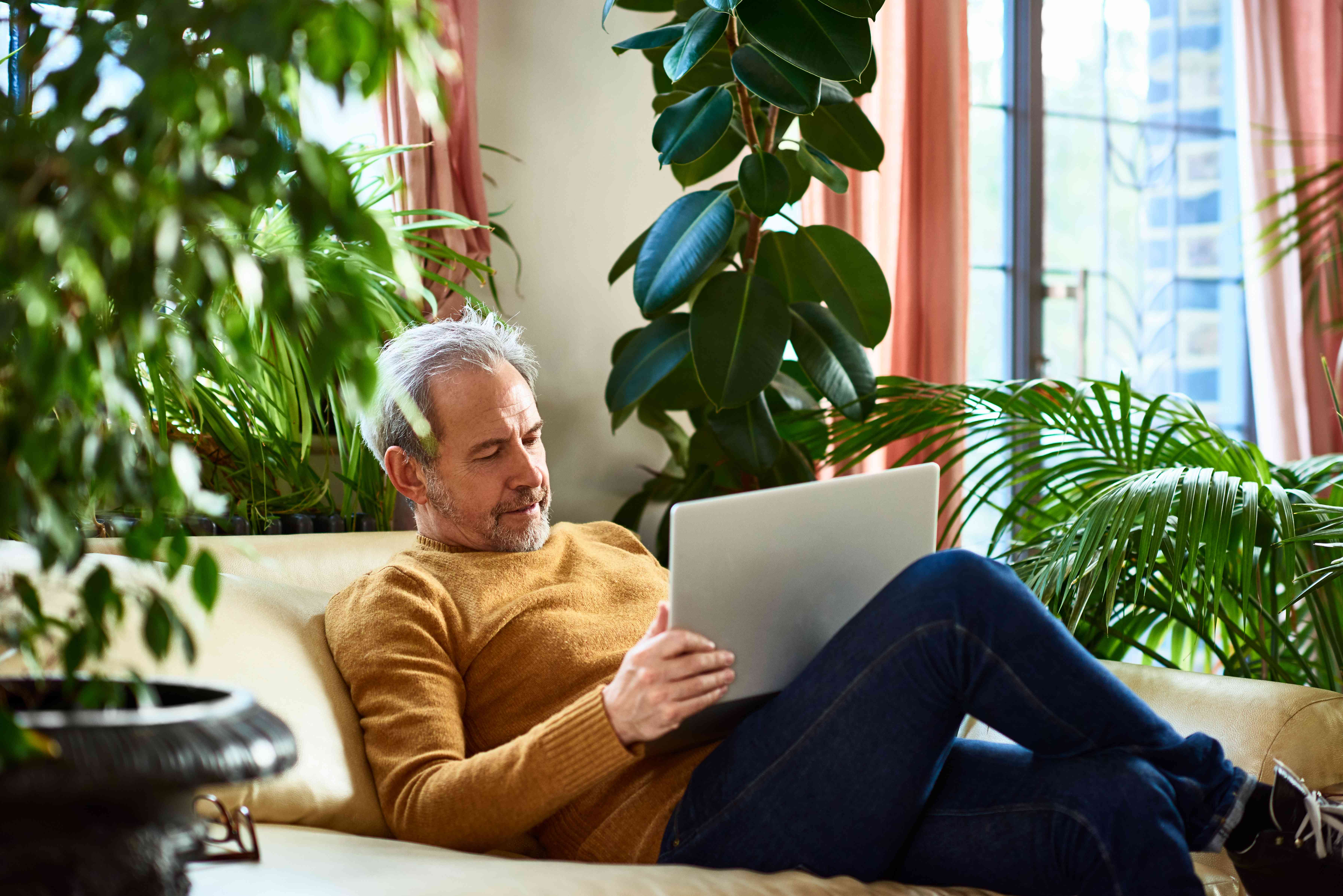 Older man relaxing on his living room couch while looking at a laptop