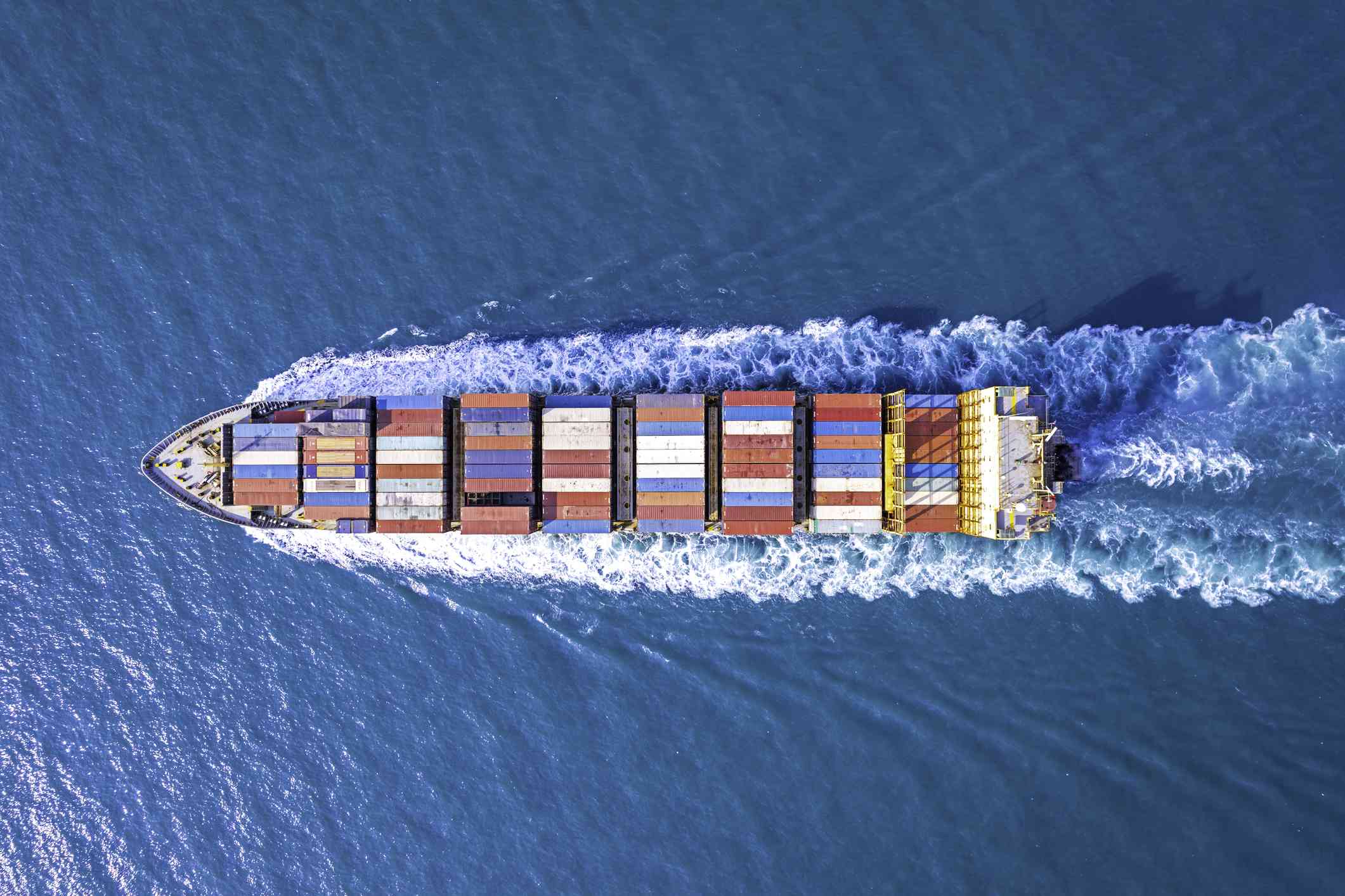 An aerial view of a ship containing cargo moving through the water.