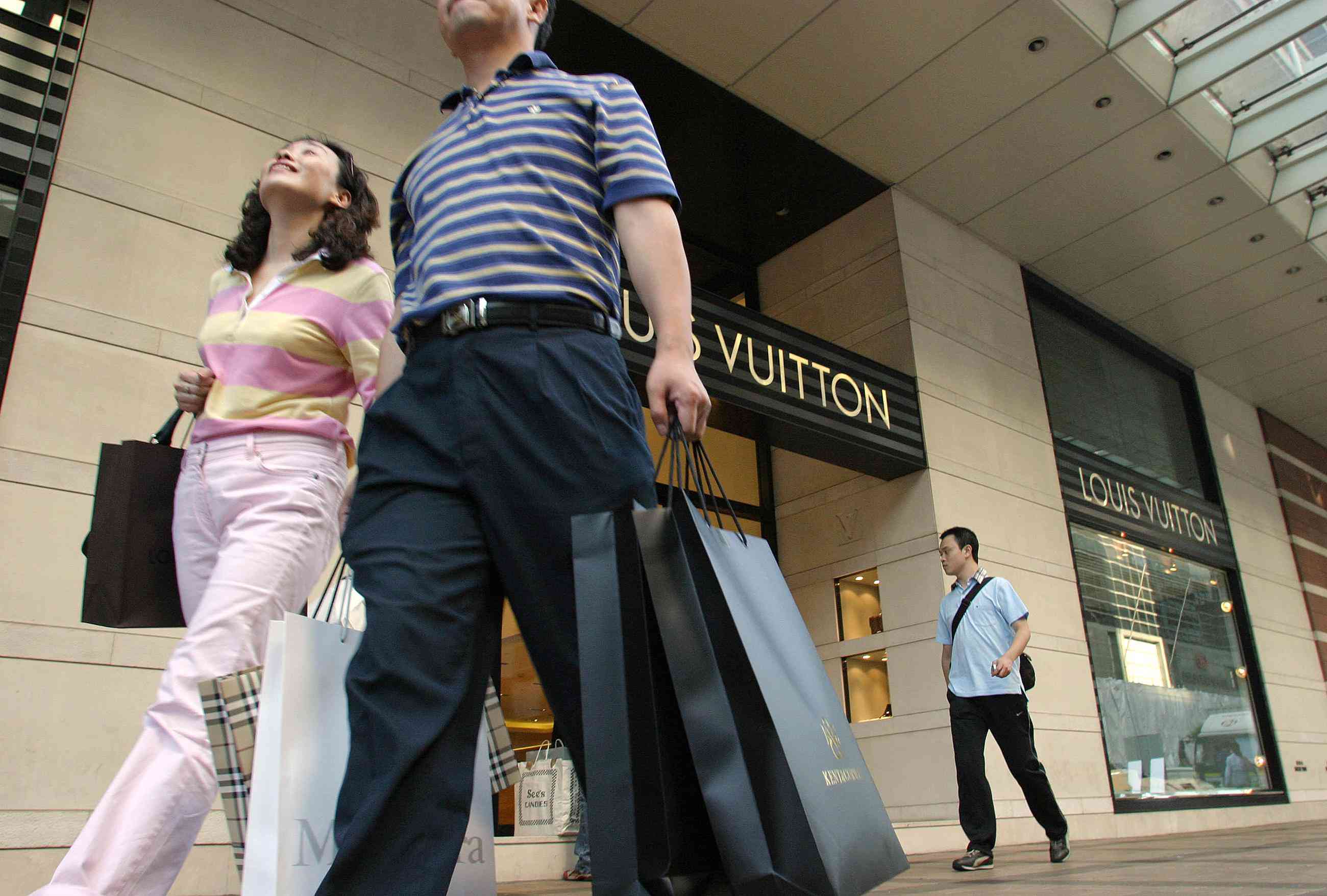 Mainland Chinese tourists loaded with shopping bags walk past a designer brand shop in the Tsim Sha Tsui area of Hong Kong