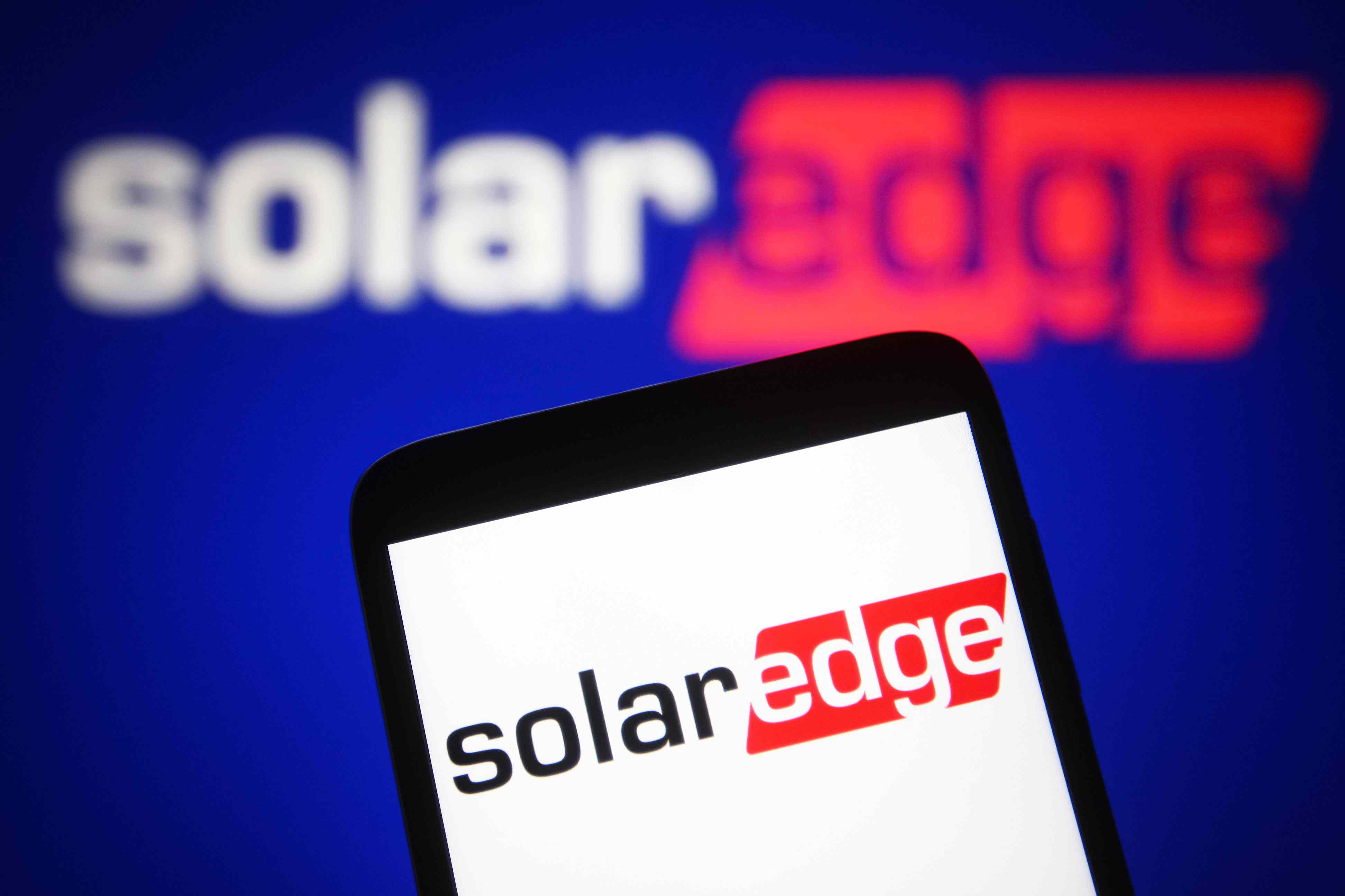 A SolarEdge Technologies logo is seen on a smartphone and a PC screen