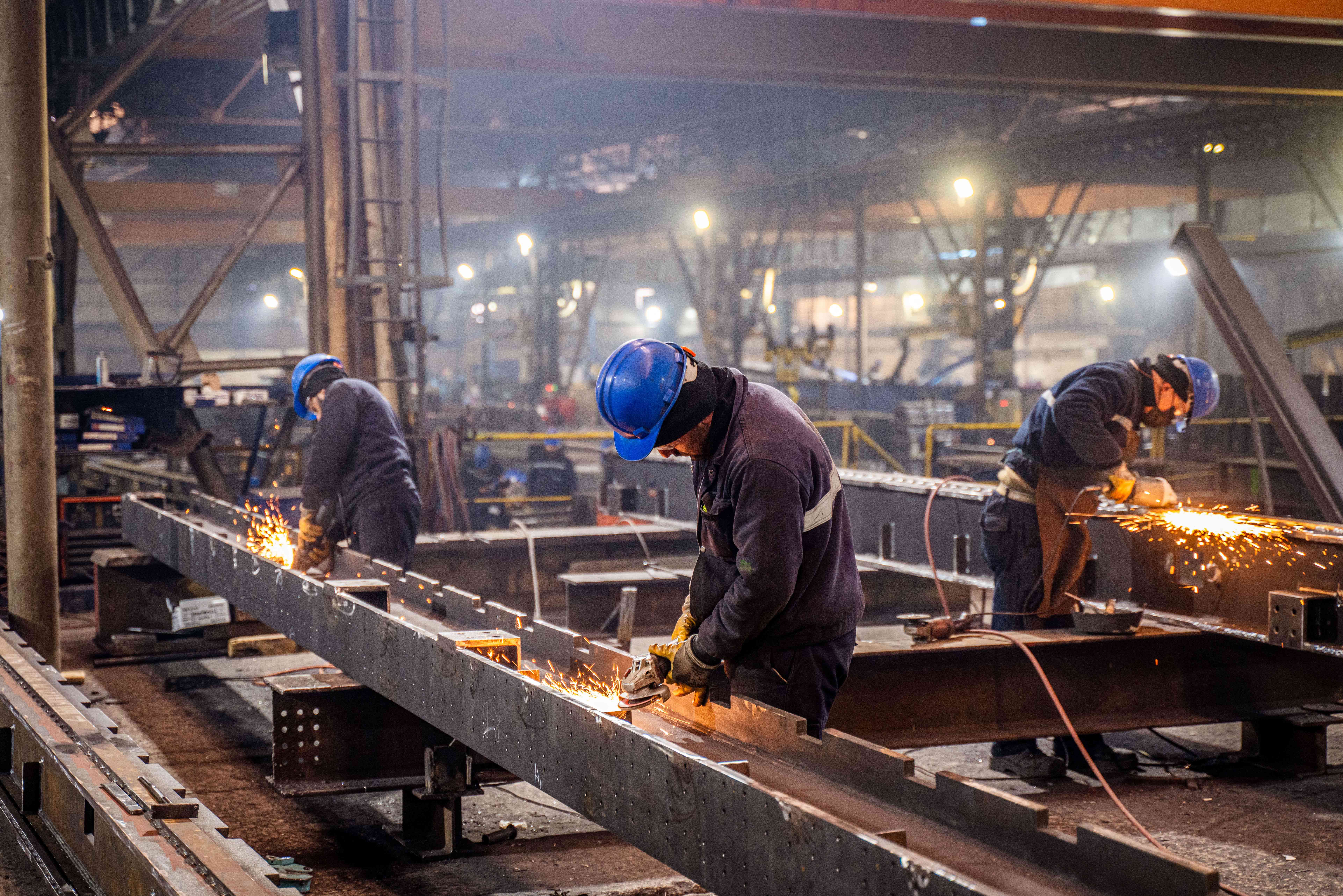 Metal workers using grinders on an assembly line