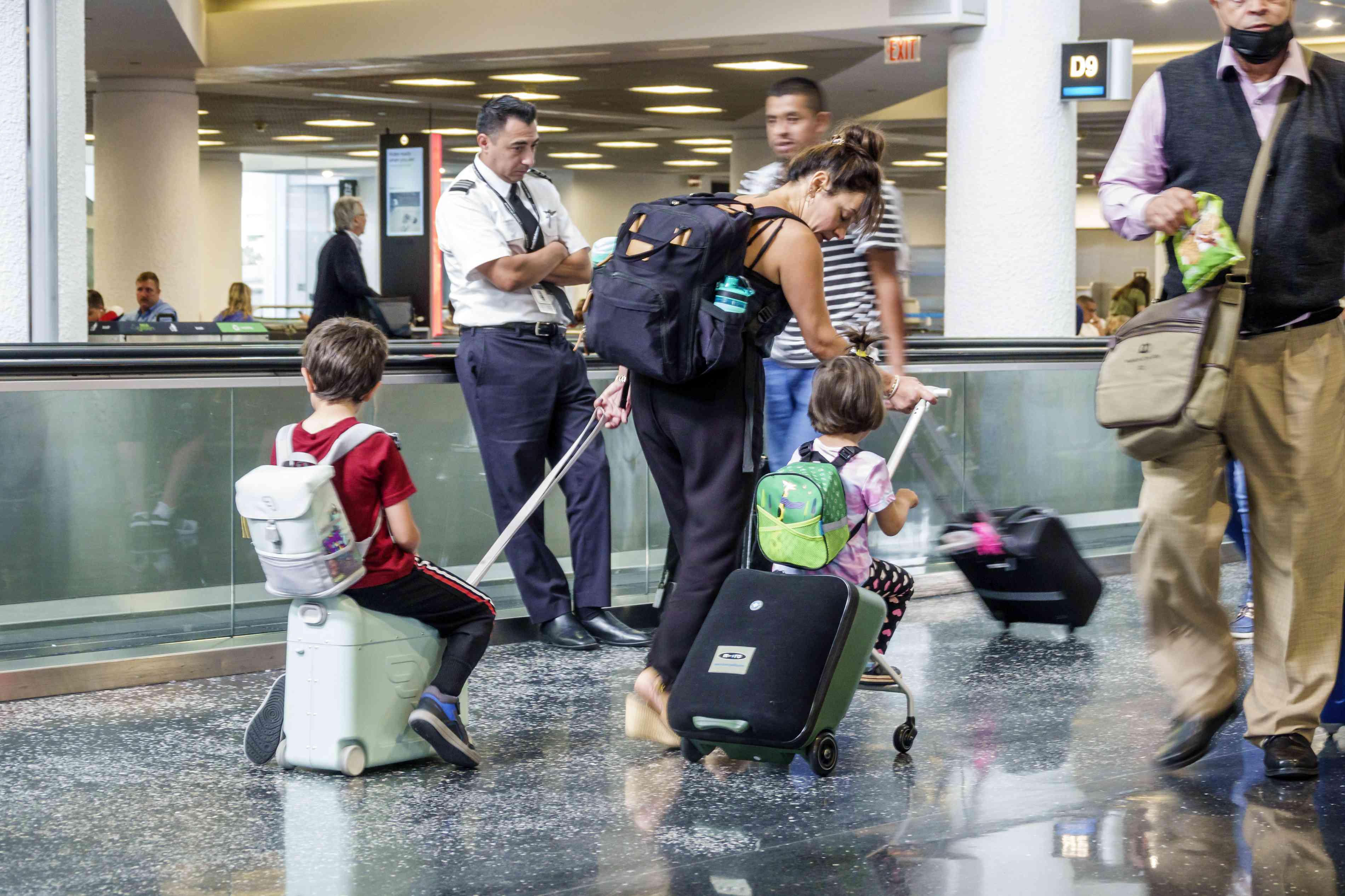 At Miami International Airport MIA terminal, passengers with children riding on rolling suitcases