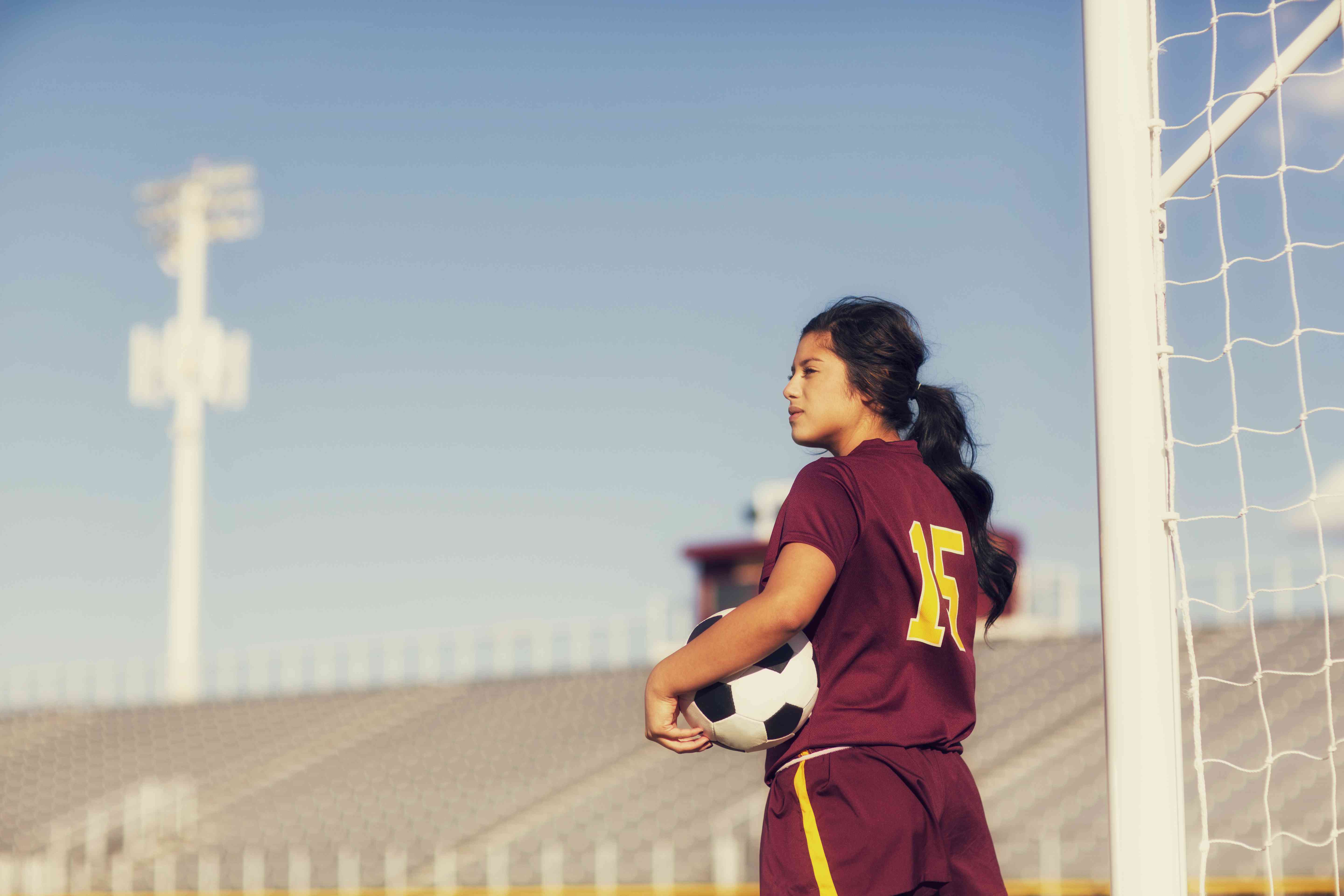 Female high school soccer player holding ball. 