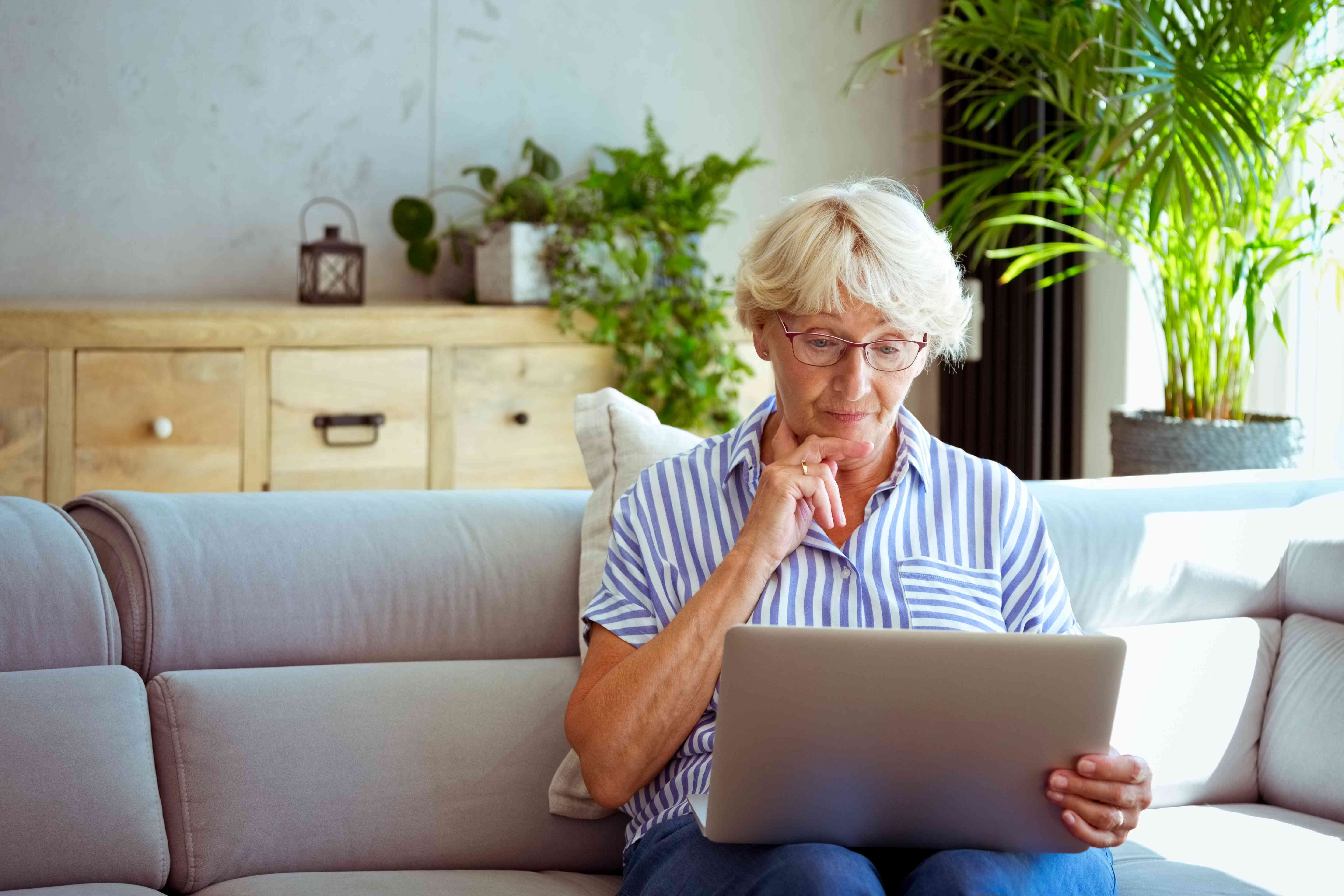 Older woman sitting on her living room couch and looking intently at a laptop screen