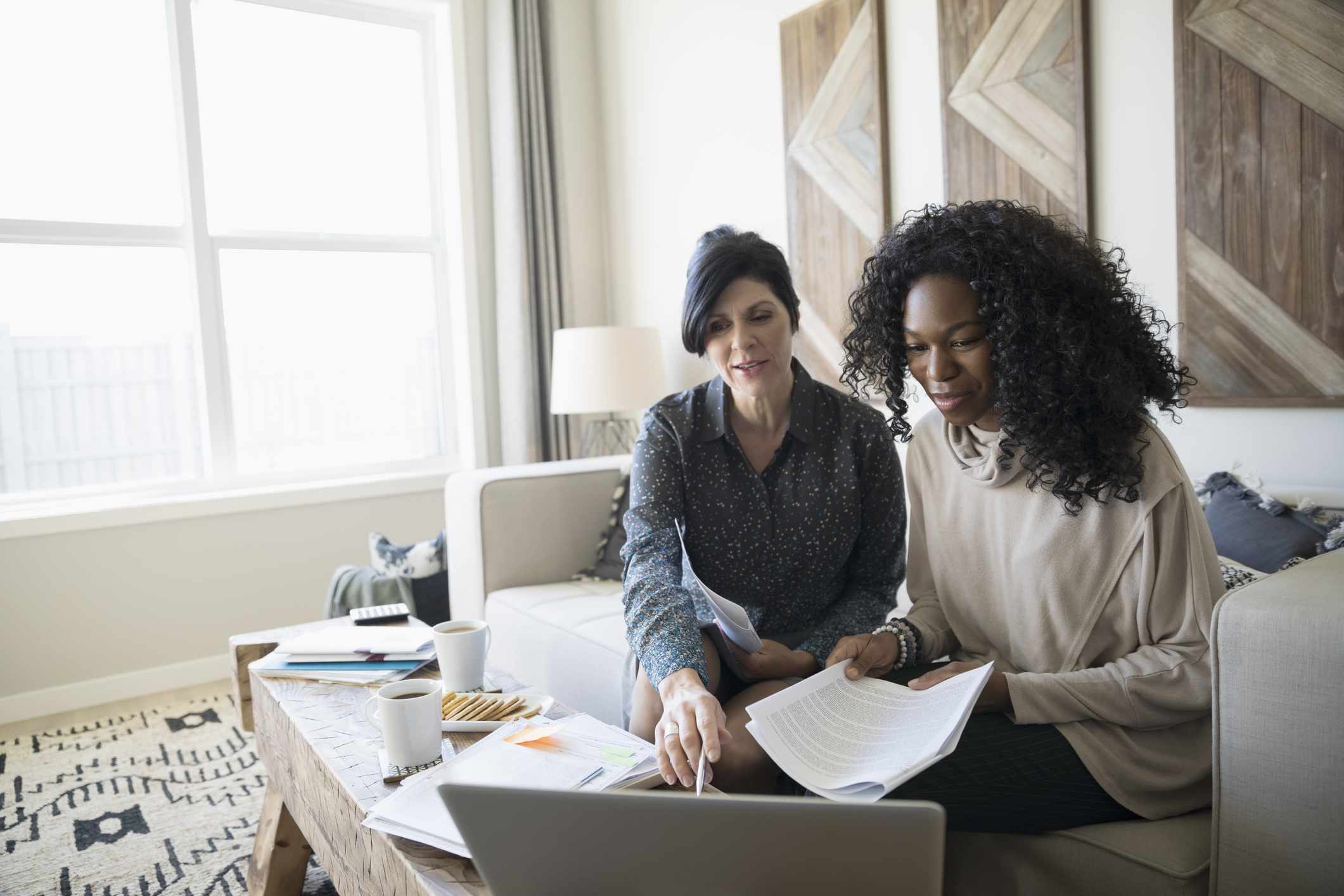 Financial advisor with laptop and paperwork meeting with woman in living room.