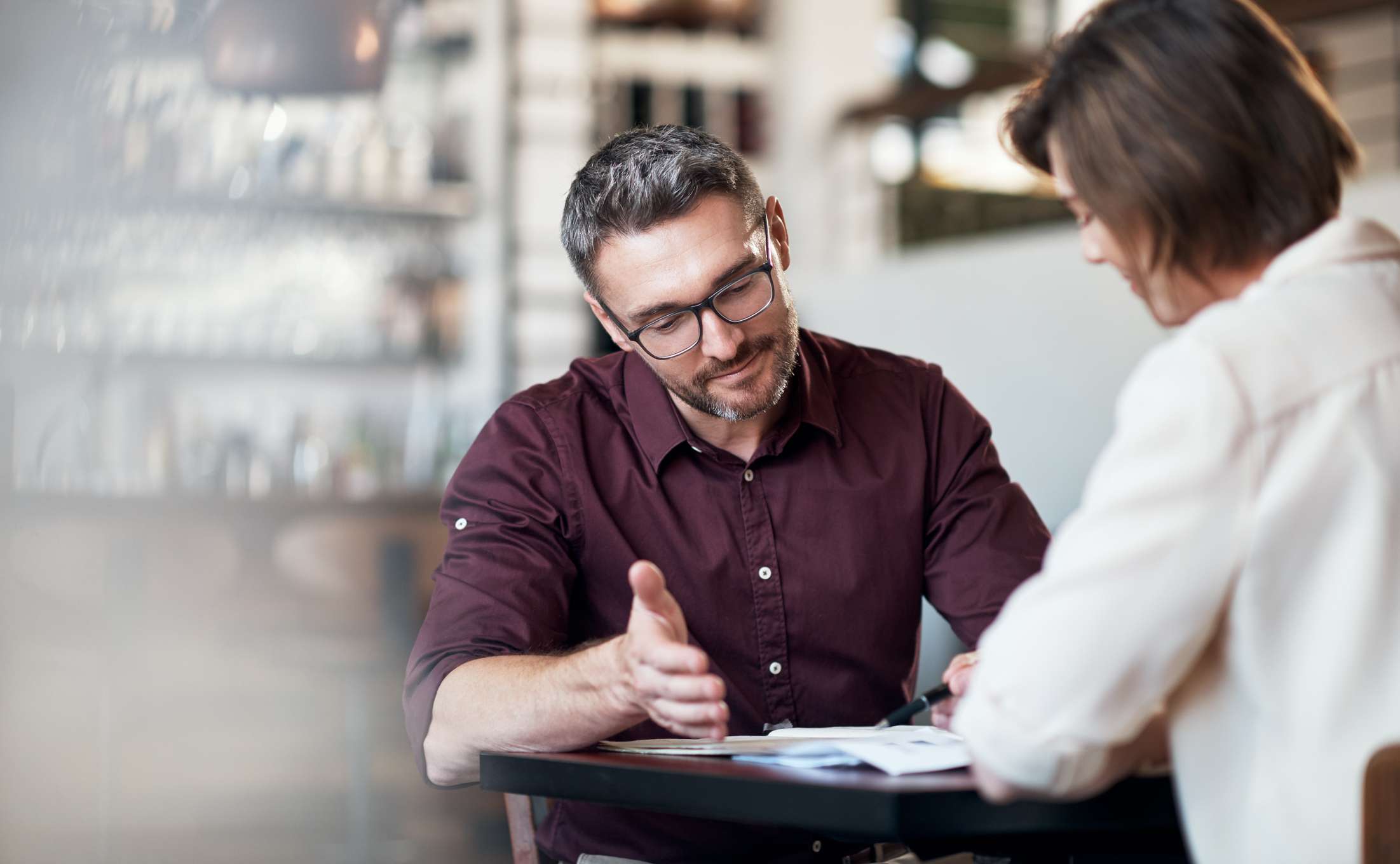 Two adults sitting at a table discuss documents.