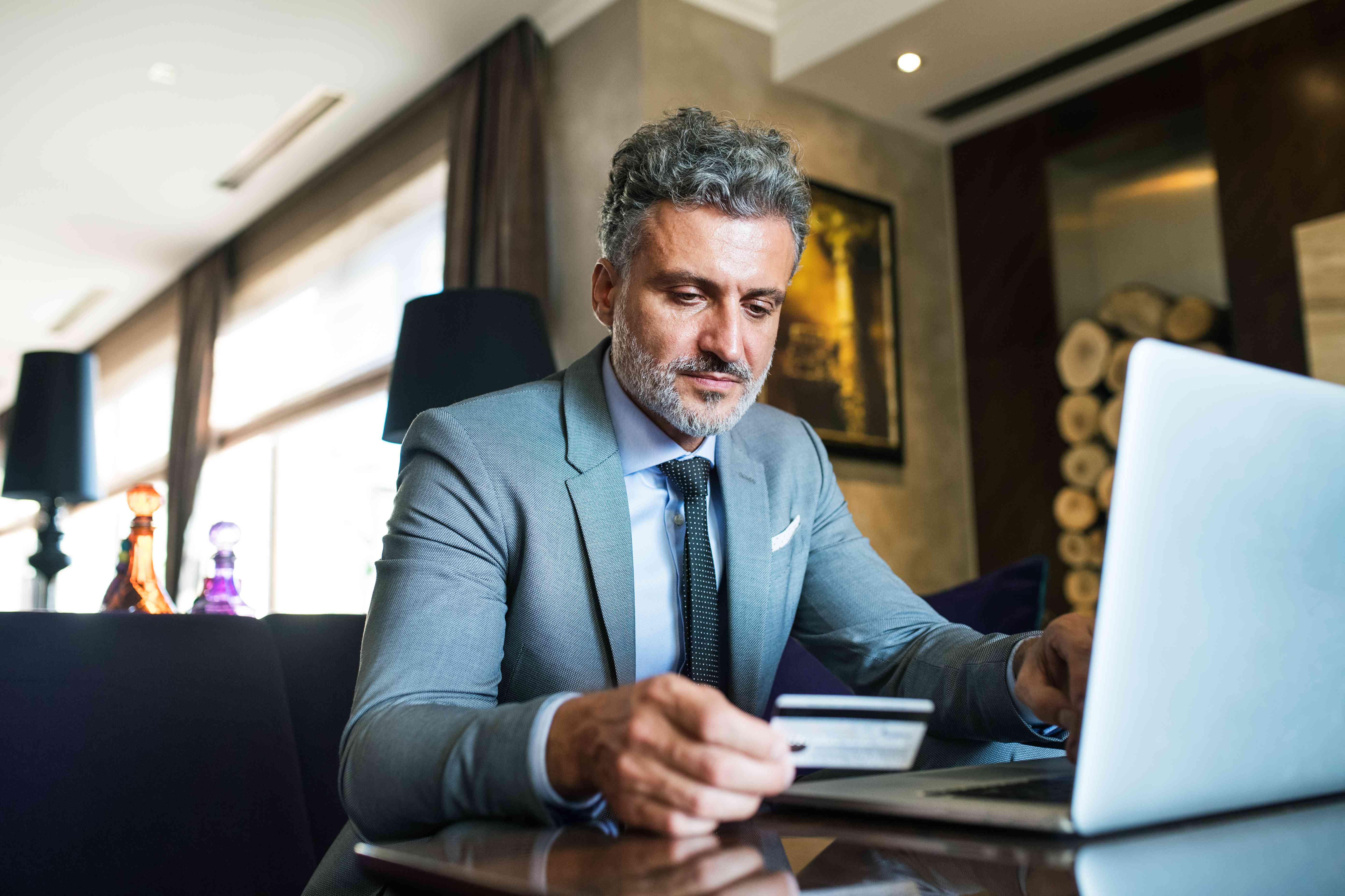 Businessman with laptop in a hotel lounge. Man holding a credit card. Internet banking. Online payment.