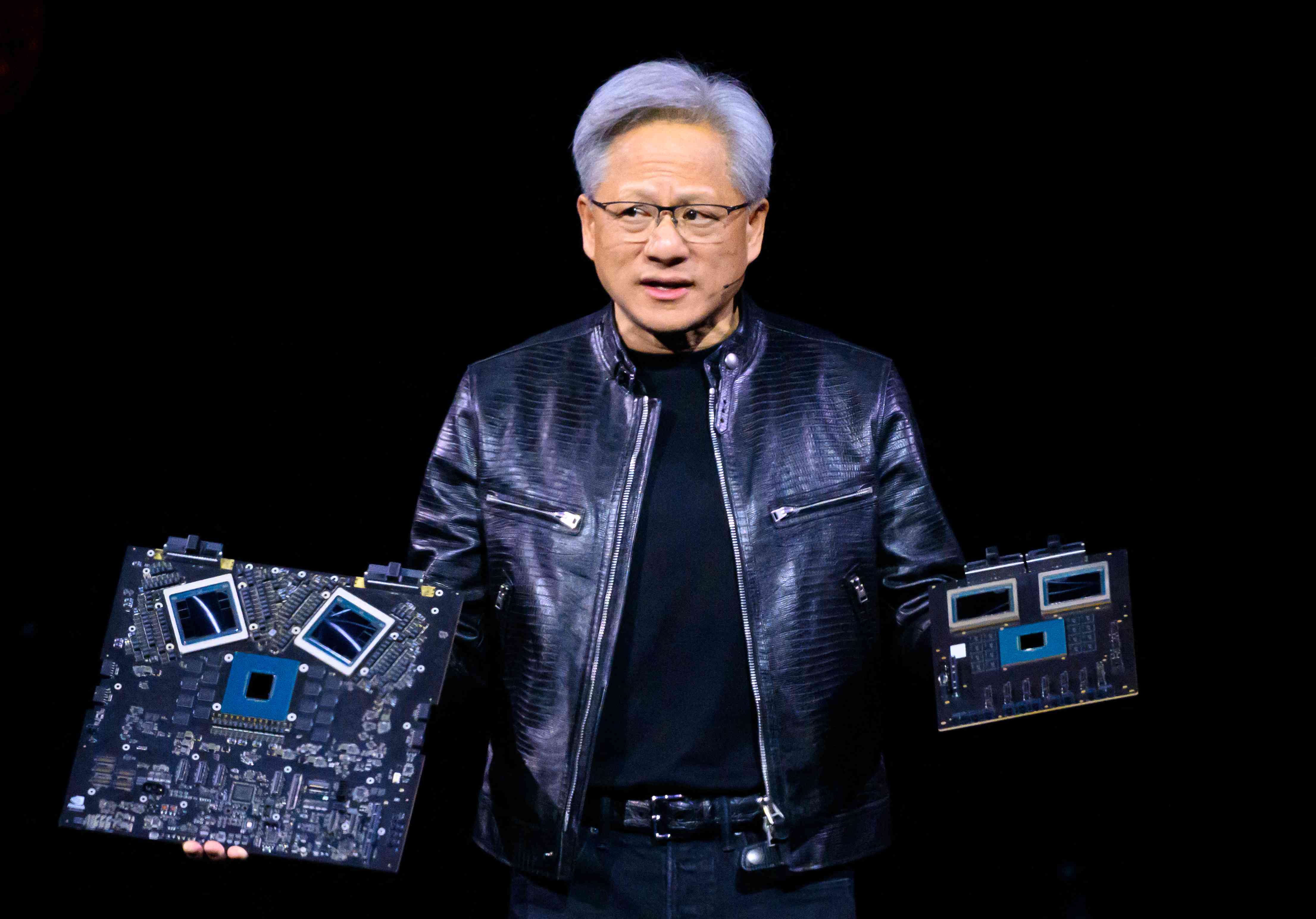 CEO Jensen Huang holds two Nvidia products while speaking on stage 