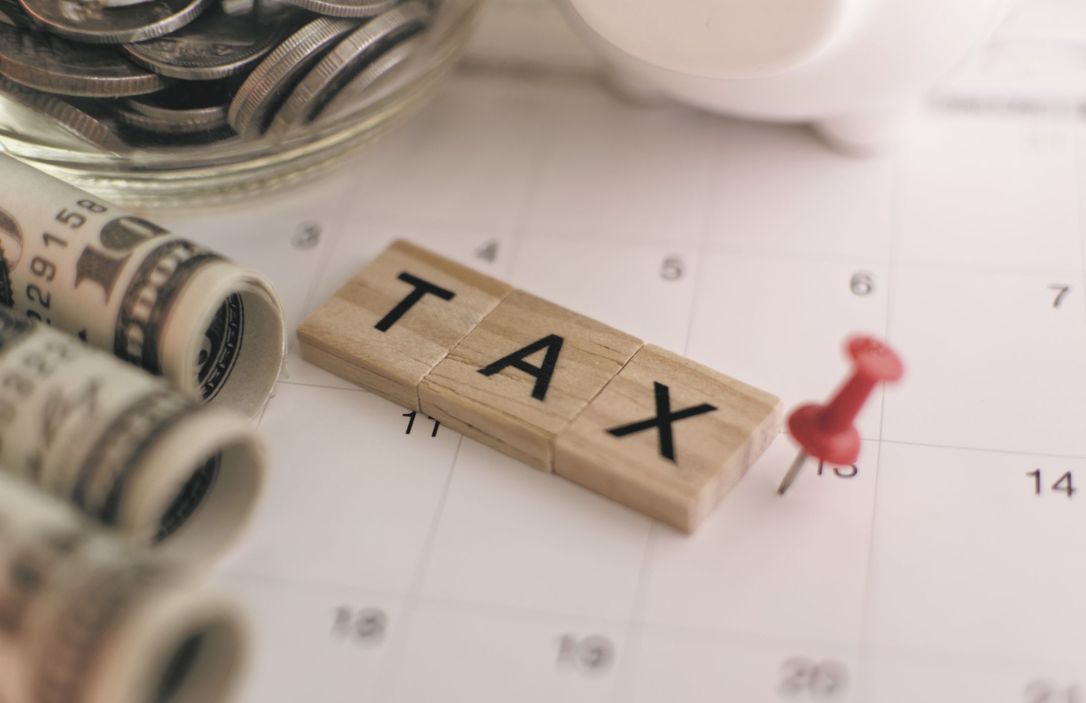 Small wooden tiles reading TAX next to money and a pushpin, all on a calendar