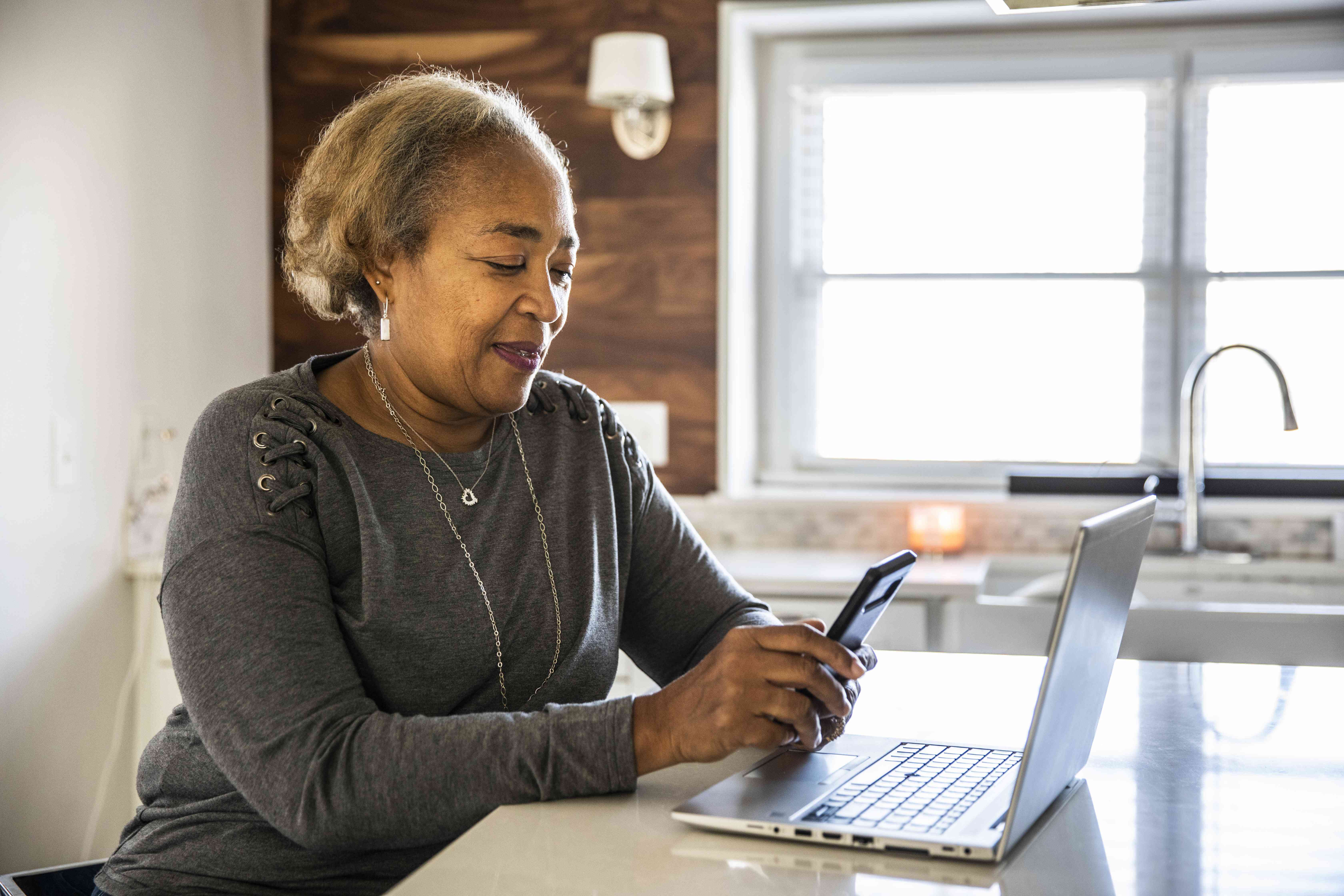 Woman working with a smartphone and laptop in a kitchen