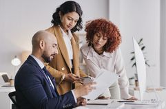 Three people stand over a desk reviewing paperwork in an office