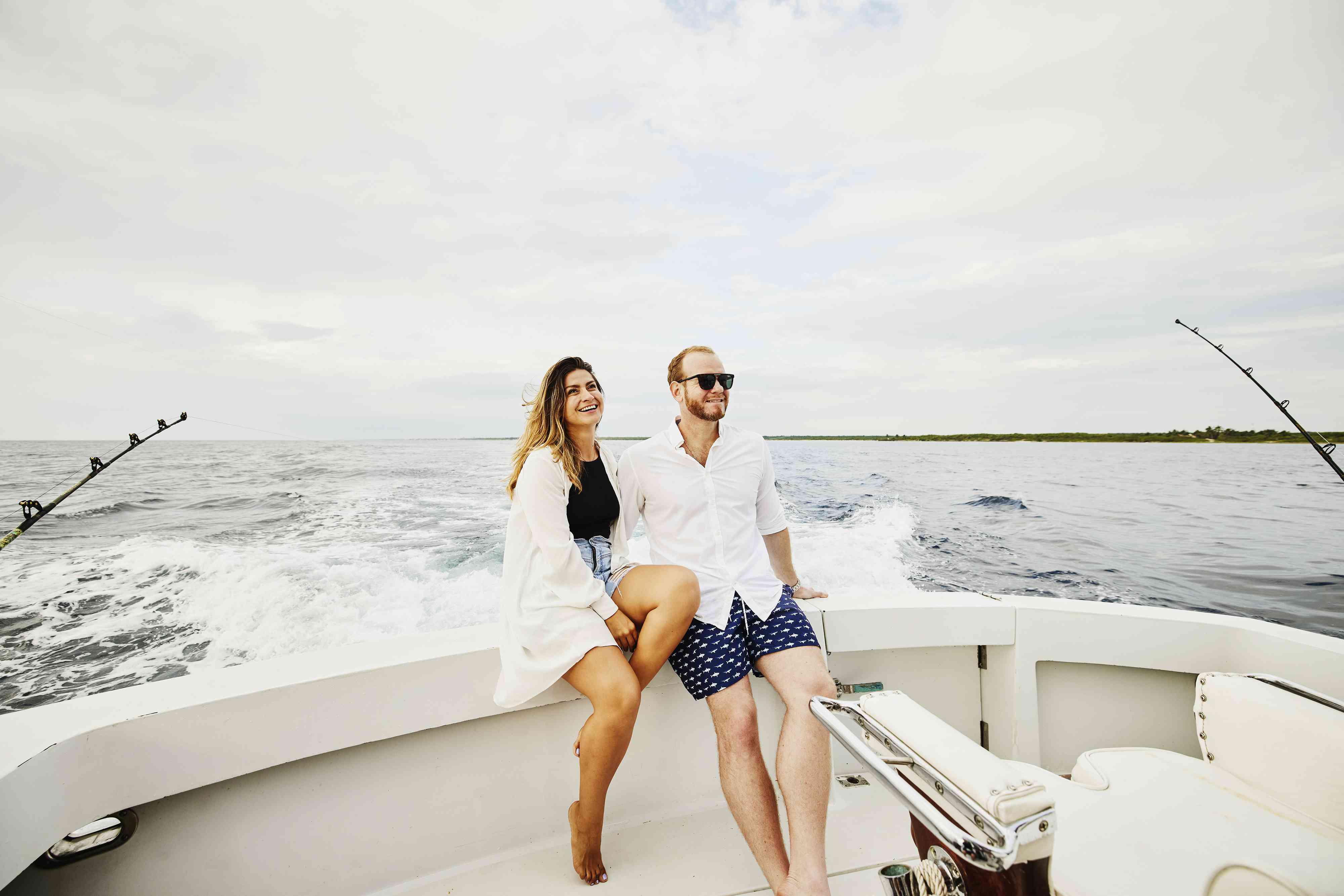 Wide shot of smiling couple sitting on stern of sport fishing boat