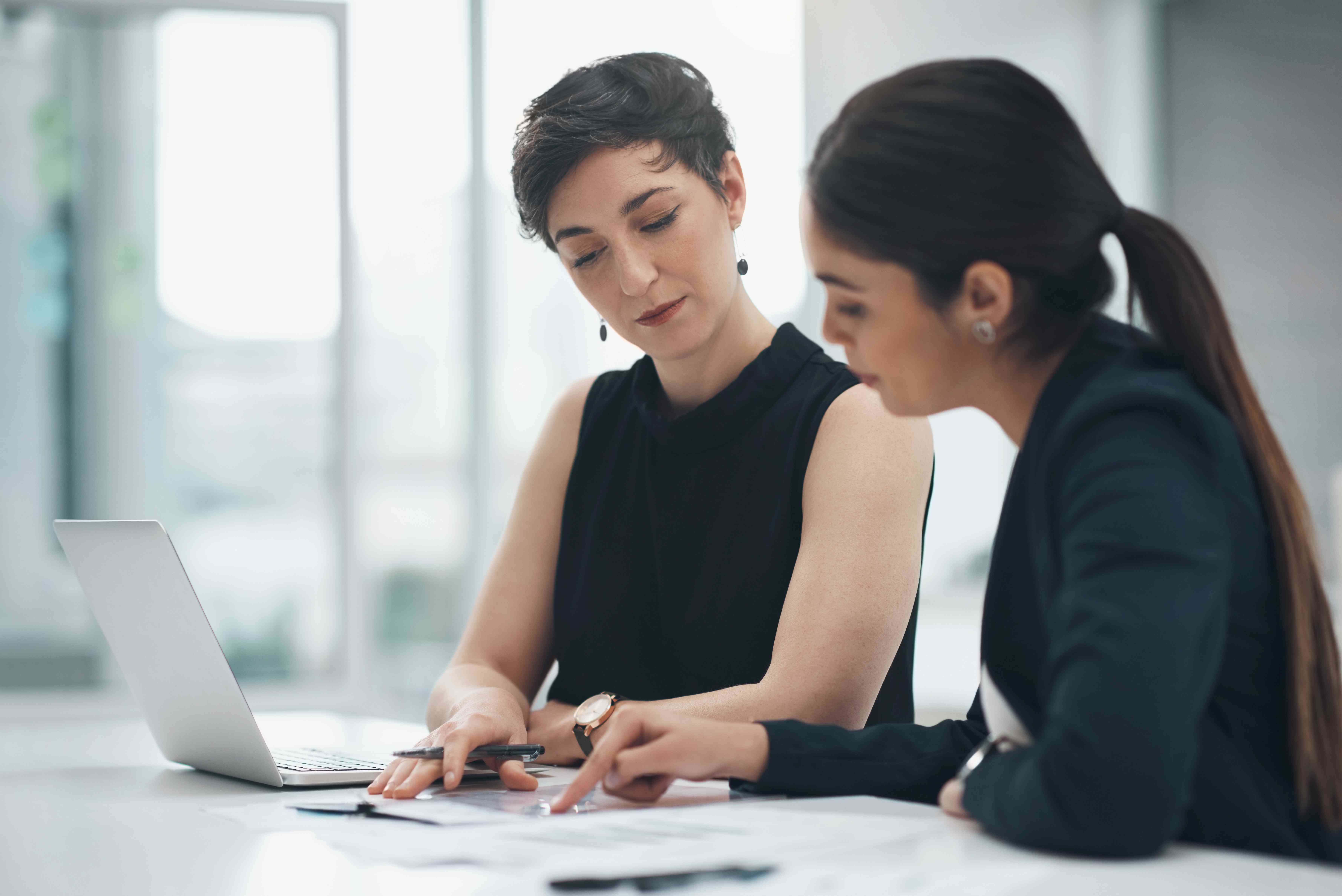 Two business women sitting at a table and talking while referring to a document