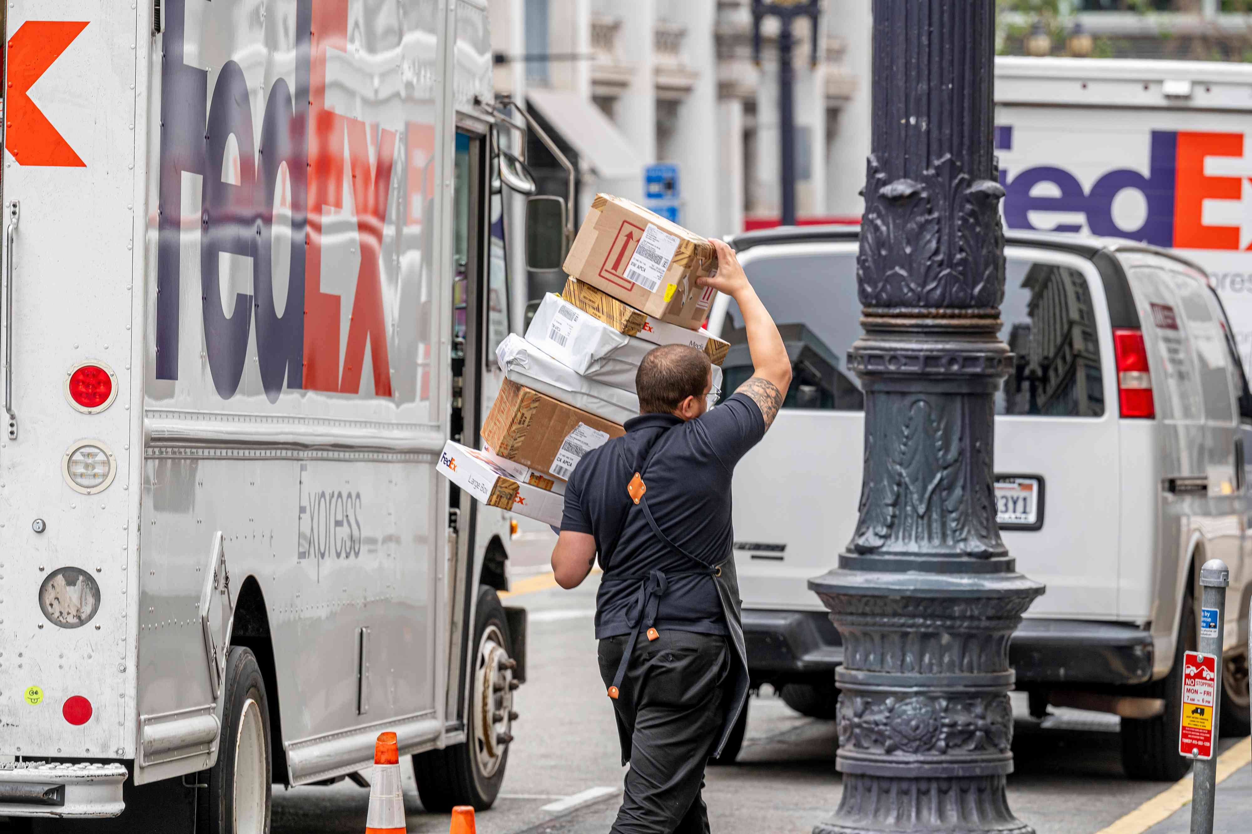 A delivery man carries packages beside a FedEx truck.