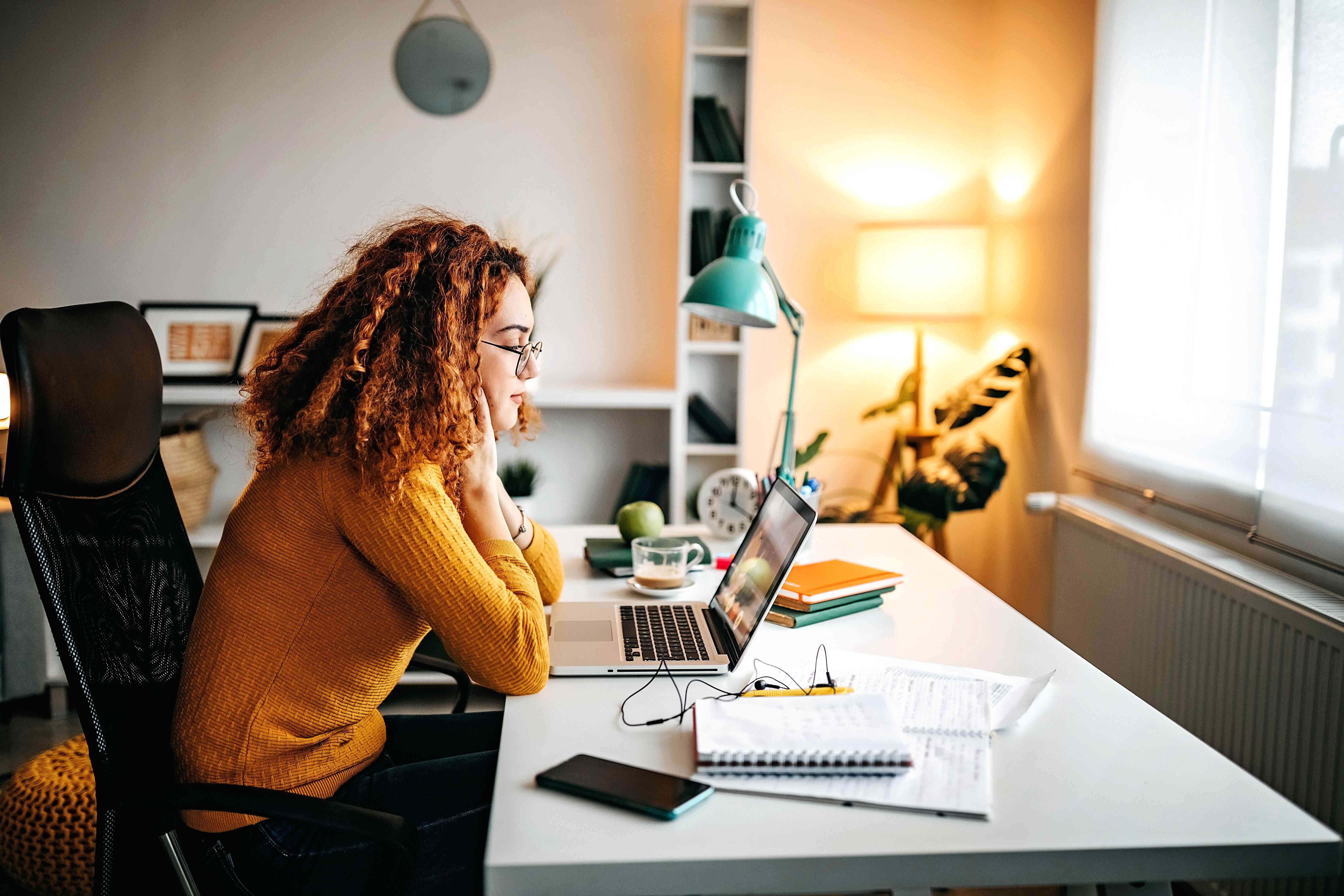 Young woman sitting at home desk studying something on her laptop screen