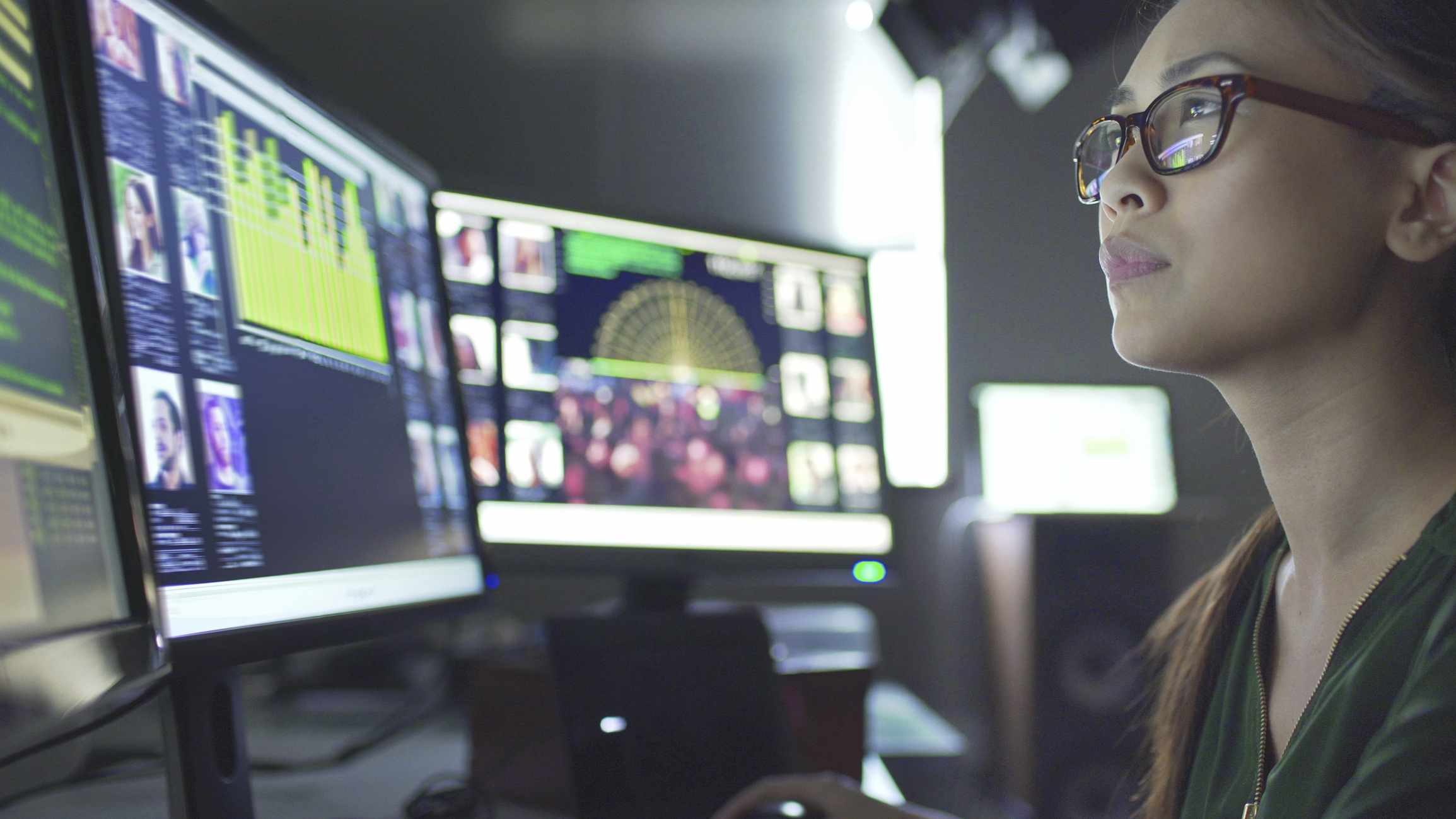 Young woman sitting at a desk with multiple computer screens.