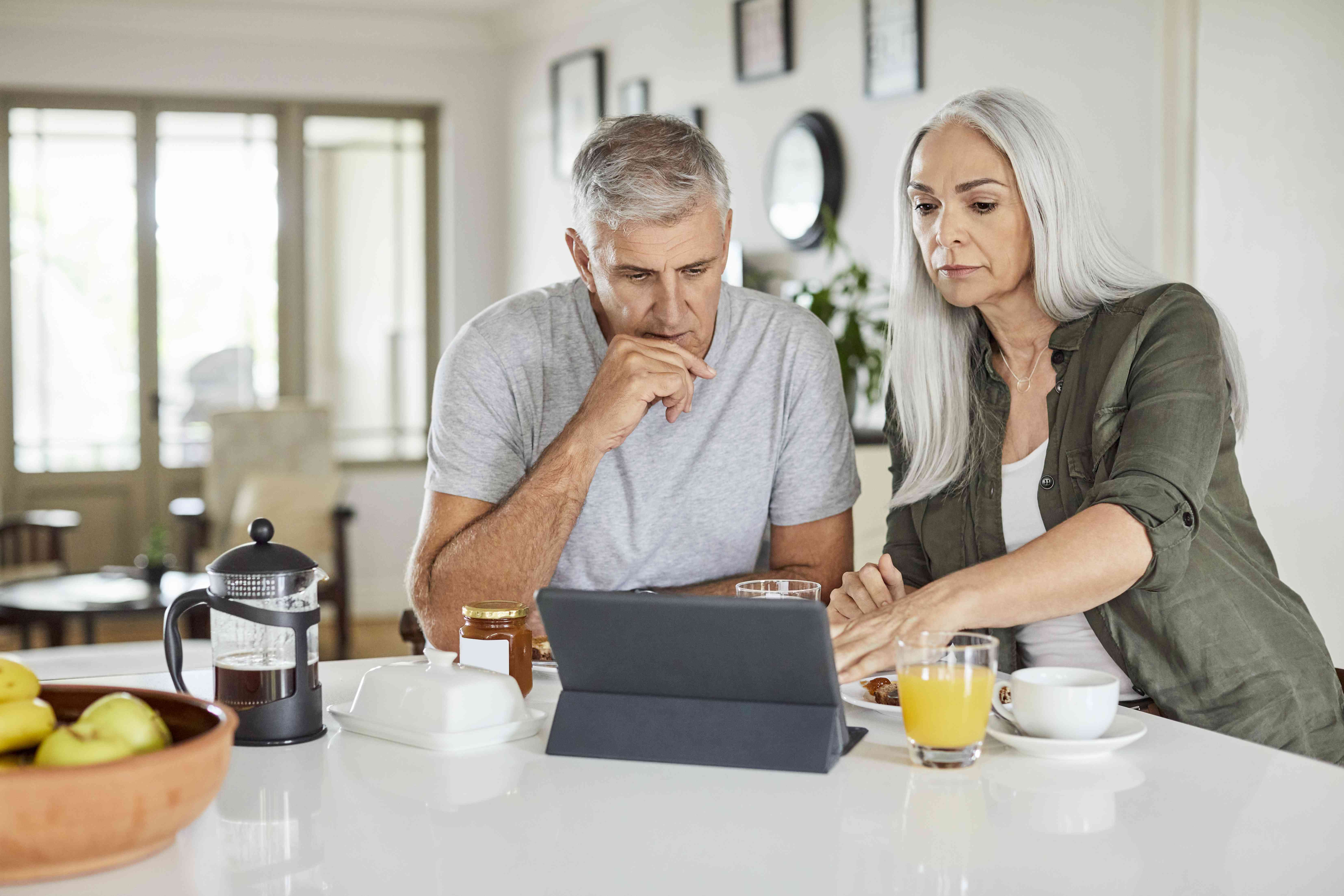 Older couple sitting at their kitchen counter and looking together at a tablet, concerned