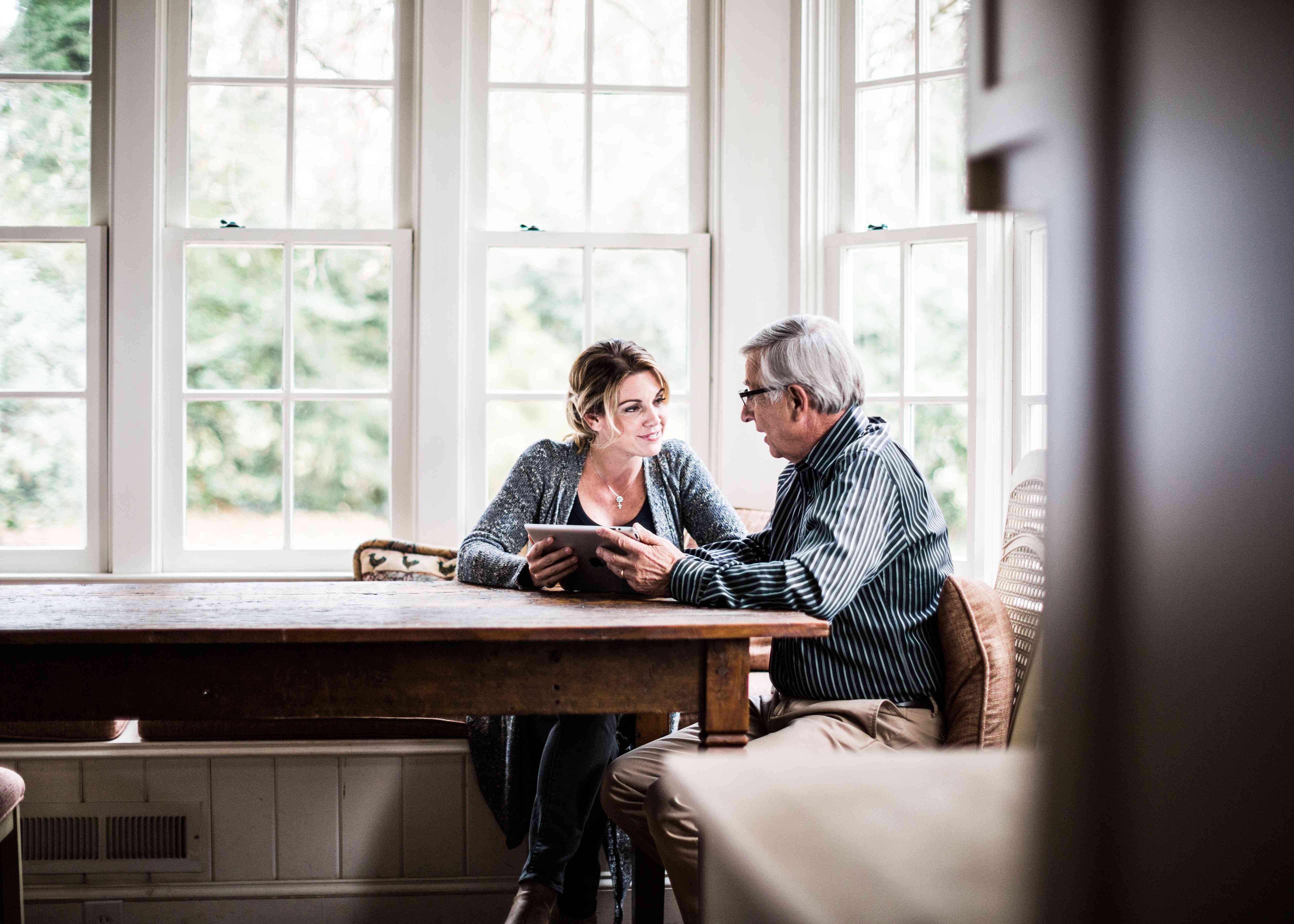 Father and daughter at a kitchen table looking at a tablet.