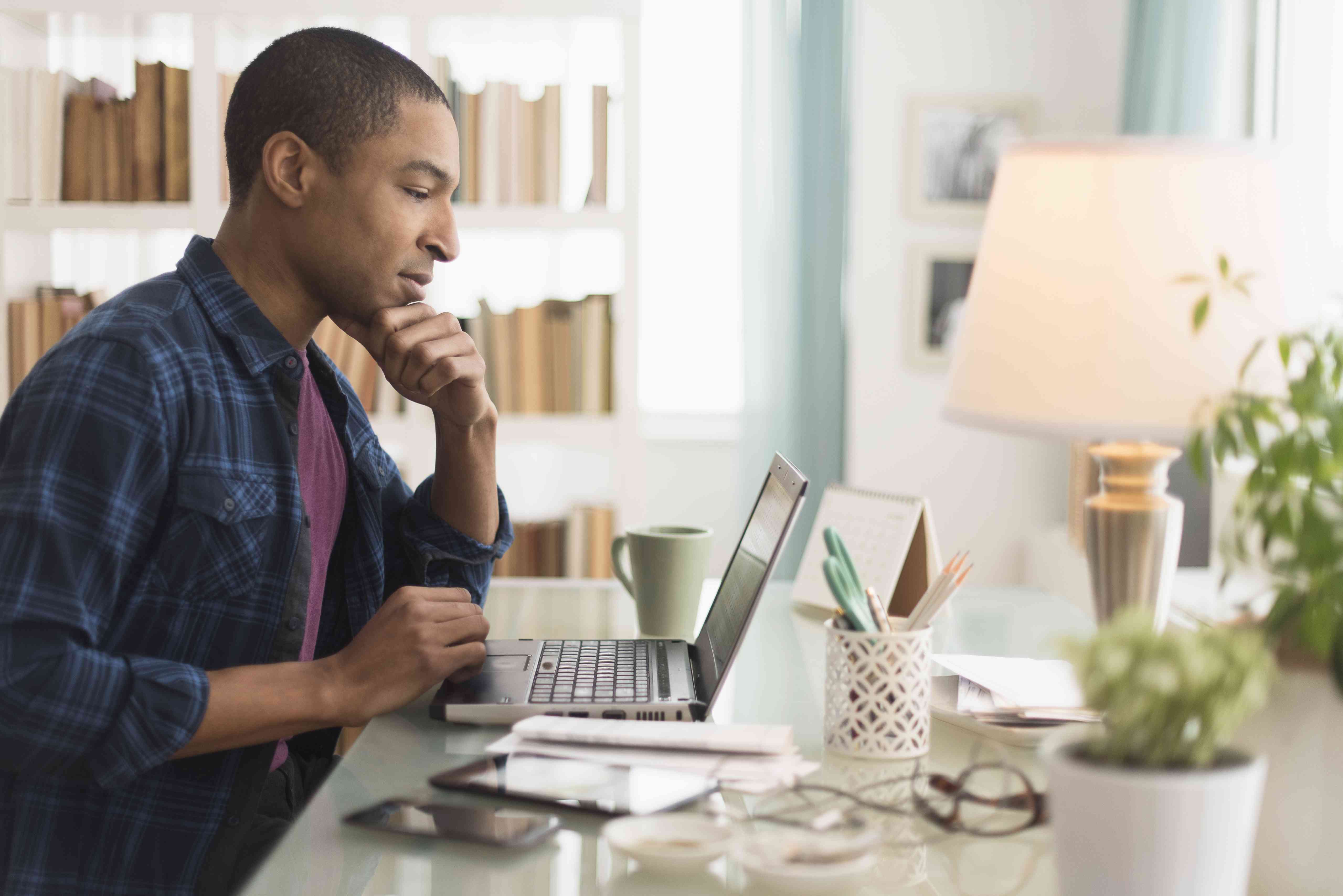 Black man in his 40s at home desk looking intently at his laptop